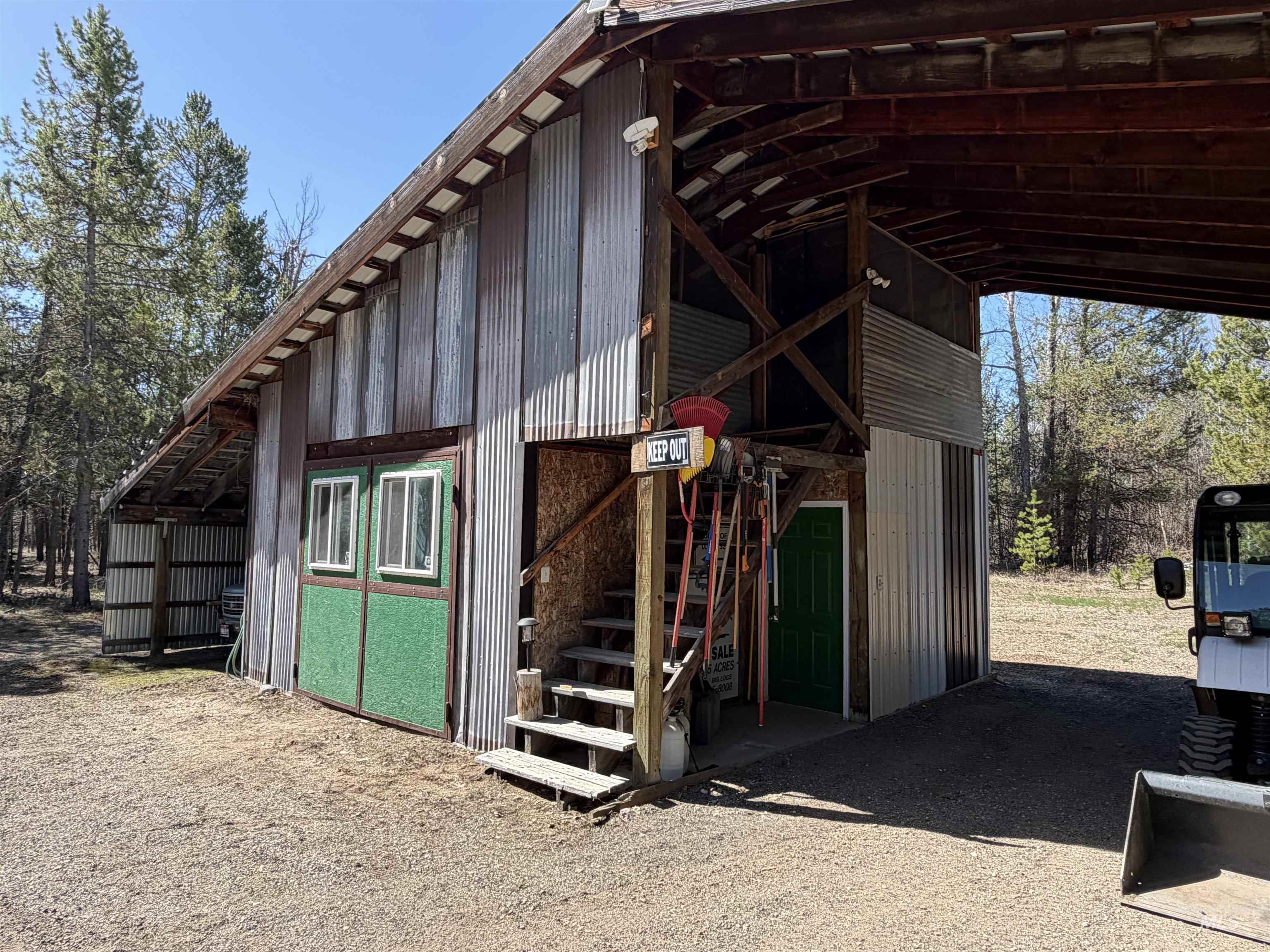 Utility building featuring corrugated metal siding, an integrated covered parking area, exterior wooden stairs, and a green entrance door