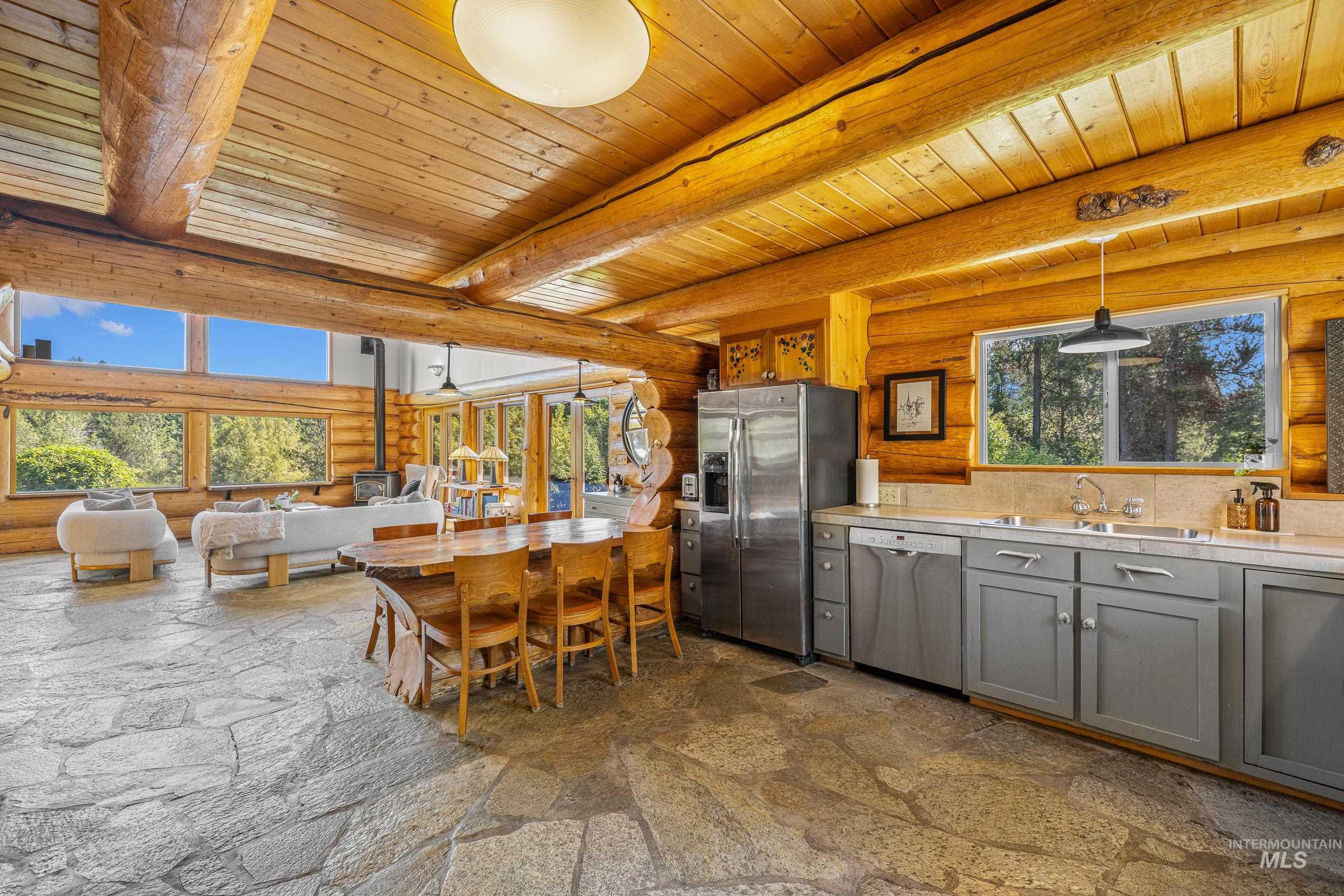 Dining area featuring log walls, healthy amount of natural light, a wooden ceiling with exposed beams, and light stone finish floors