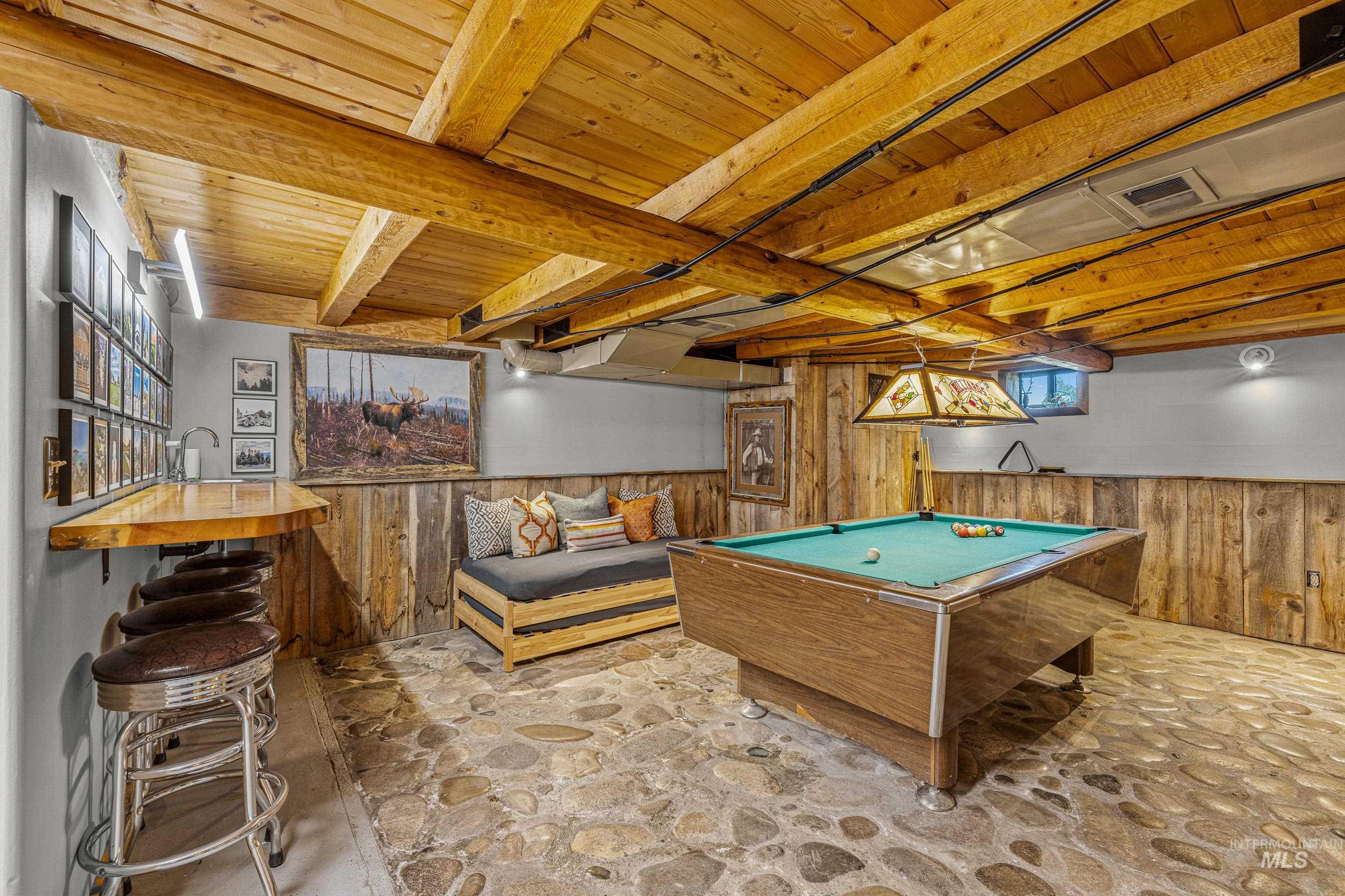 Game room with wood walls, pool table, stone flooring, wainscoting, and a wood ceiling with exposed beams