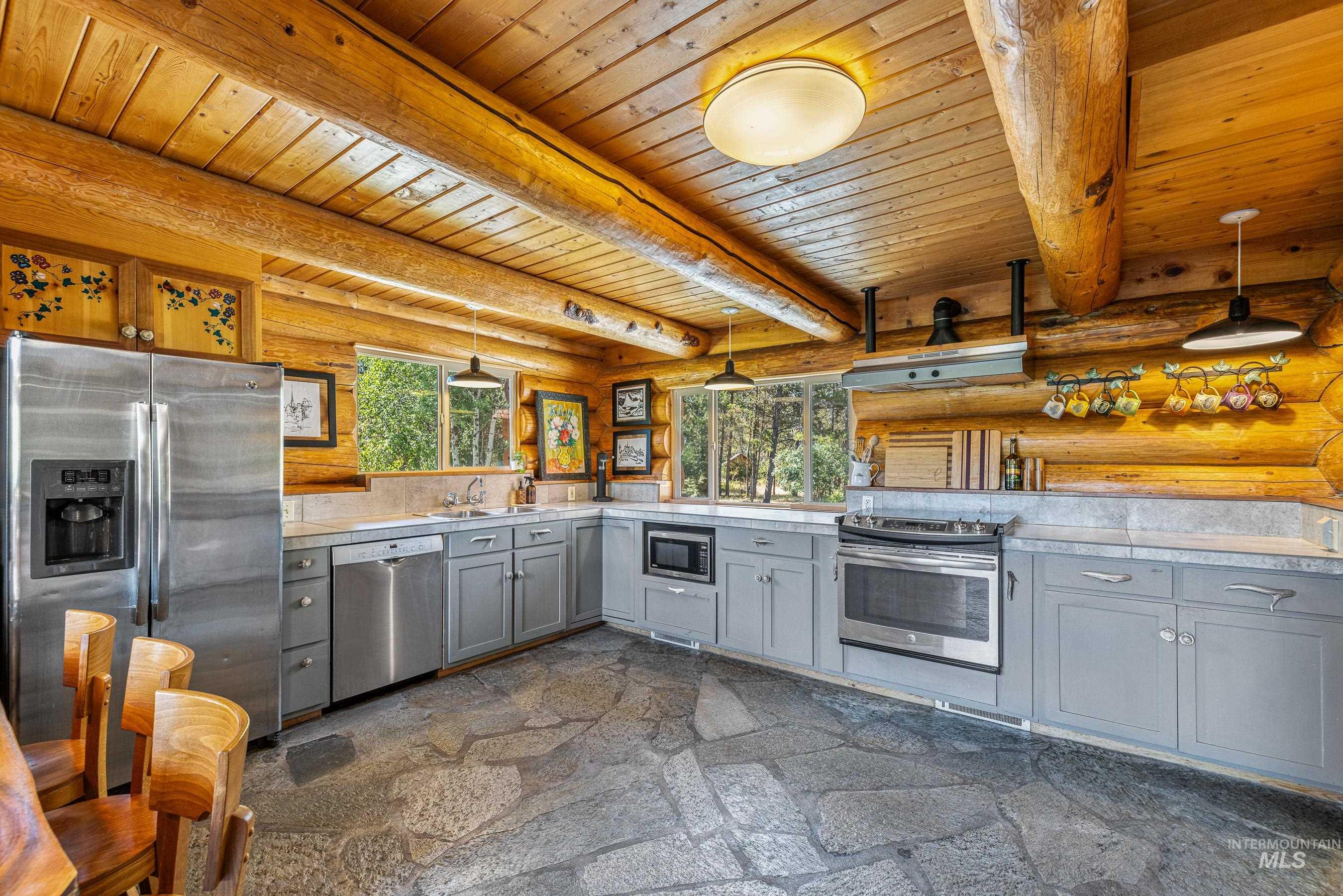 Kitchen with log walls, appliances with stainless steel finishes, healthy amount of natural light, gray cabinets, and a wooden ceiling with exposed beams