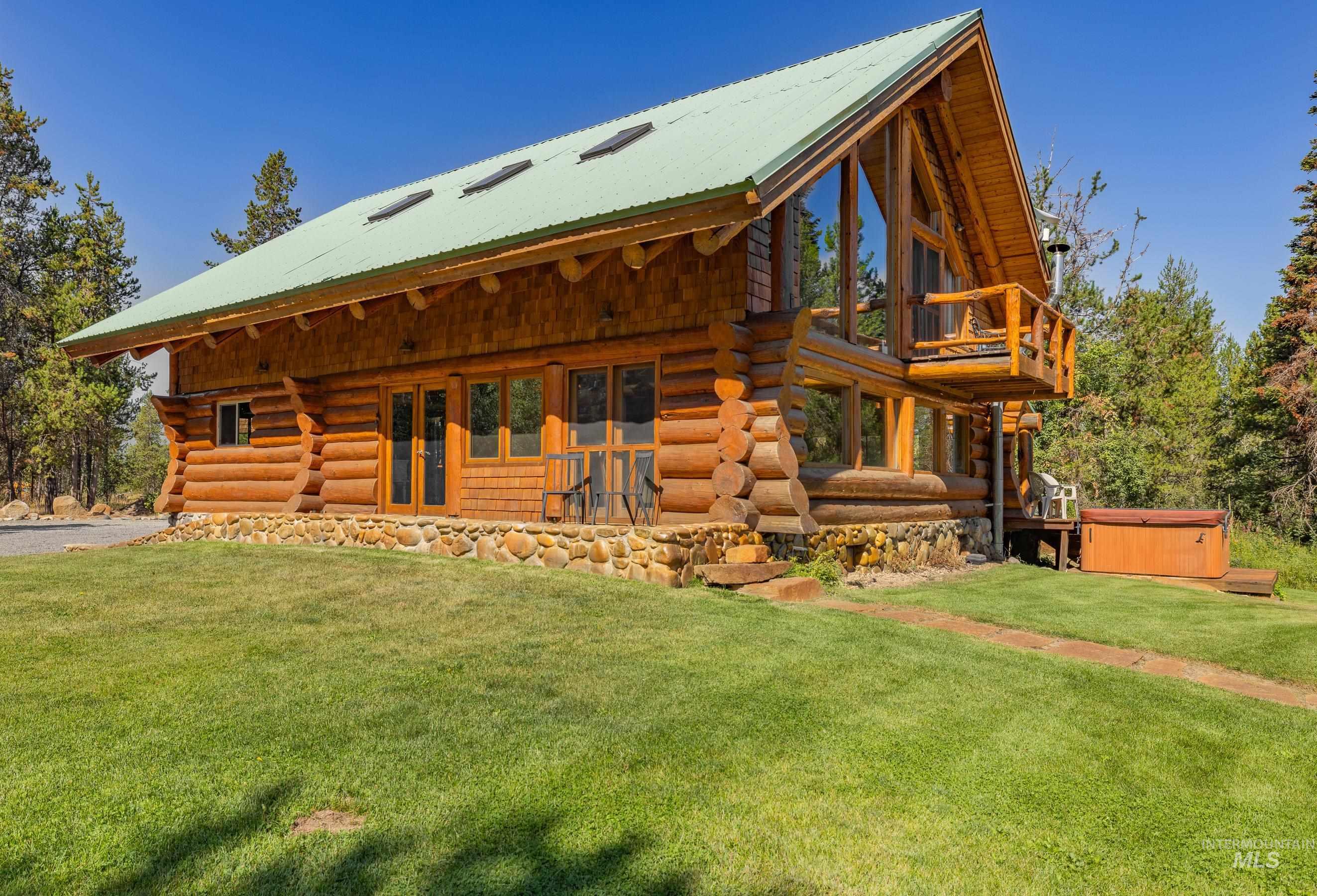 Back of house with a hot tub, log exterior, a lawn, and a metal roof