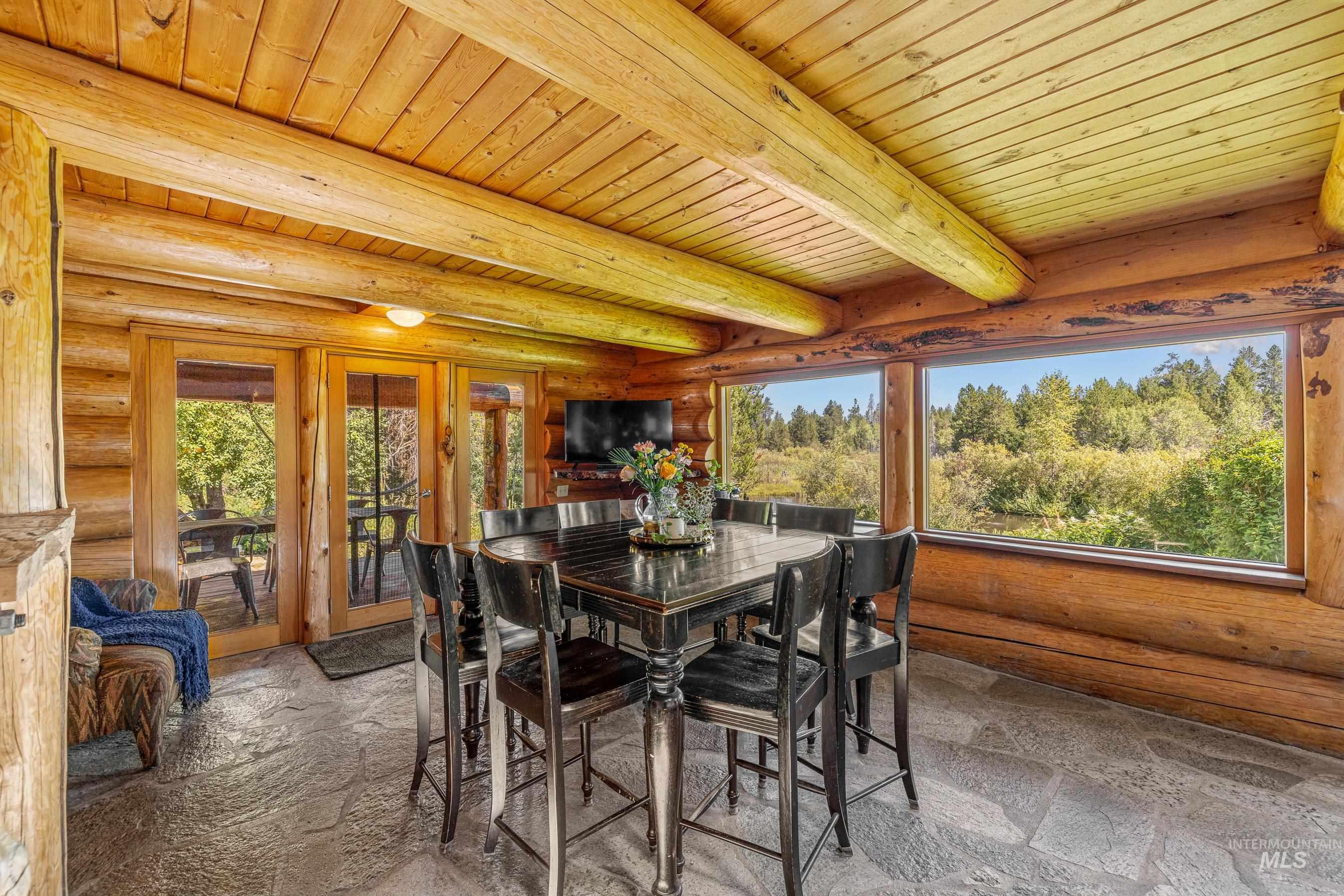 Dining area featuring log walls, stone tile floors, and a wooden ceiling with exposed beams