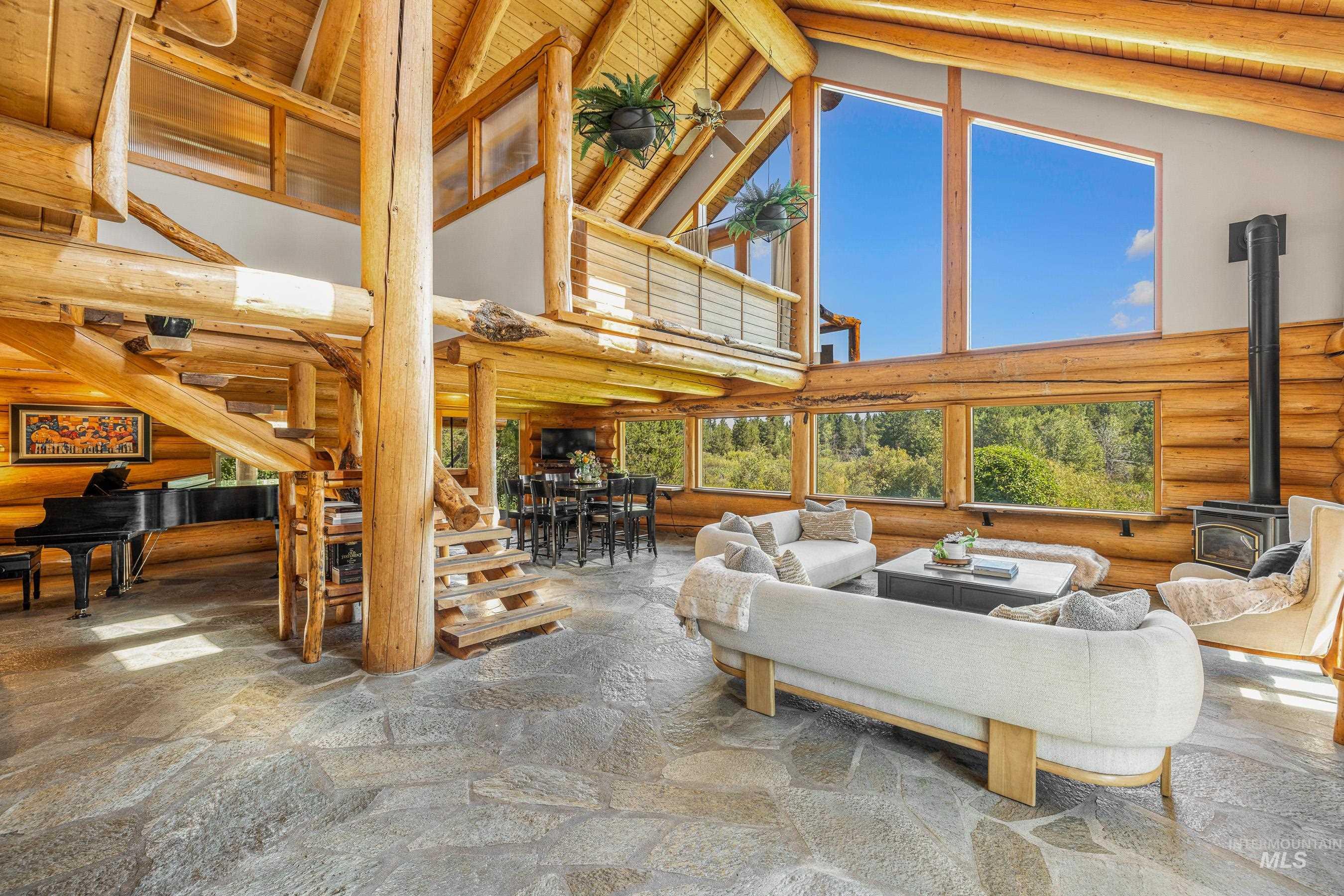 Living room featuring high vaulted ceiling, a wood stove, a wood ceiling with exposed beams, log walls, and stone finish flooring
