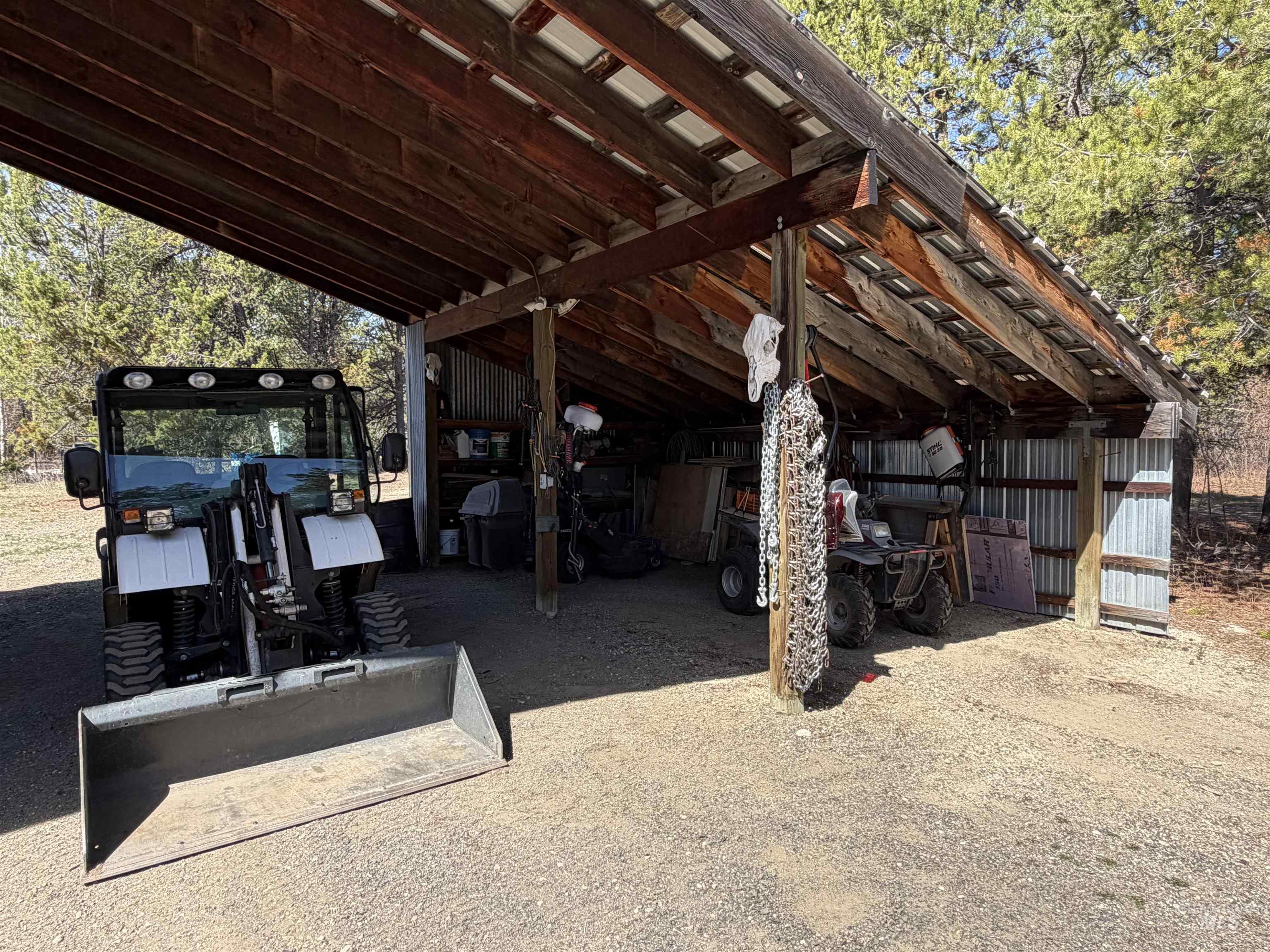 Open-sided covered structure featuring a corrugated metal roof, exposed wood beams, and a gravel floor