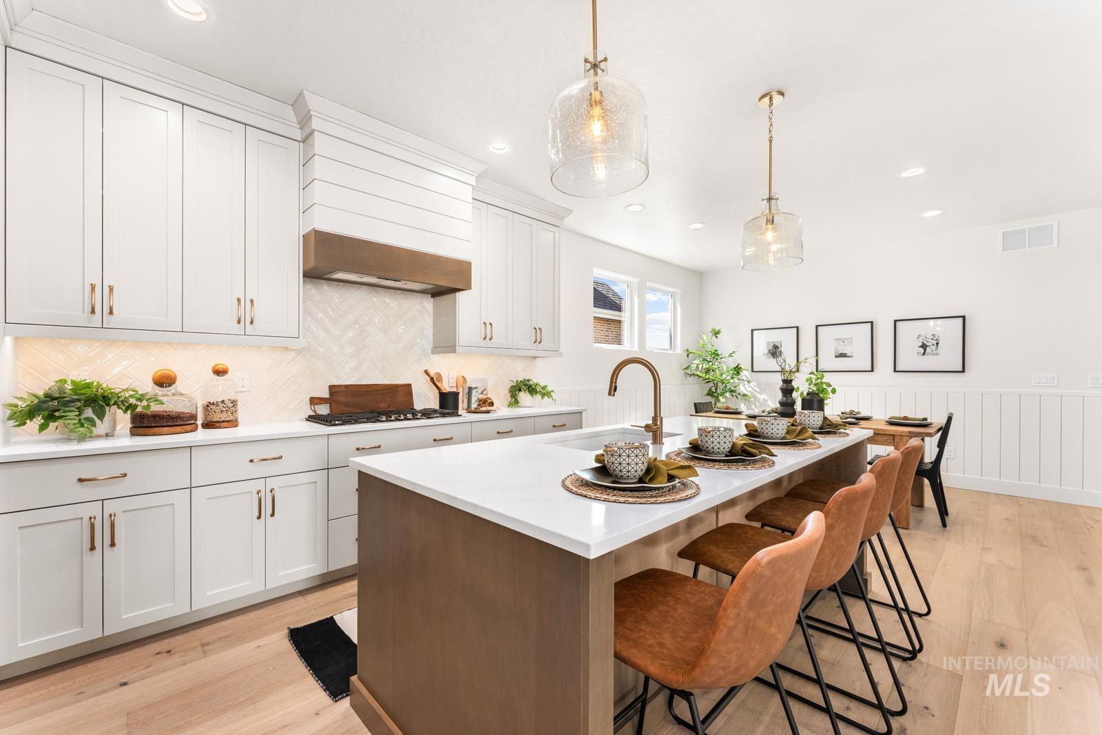 Kitchen featuring an island with sink, a breakfast bar area, light wood-style flooring, light stone counters, and hanging light fixtures