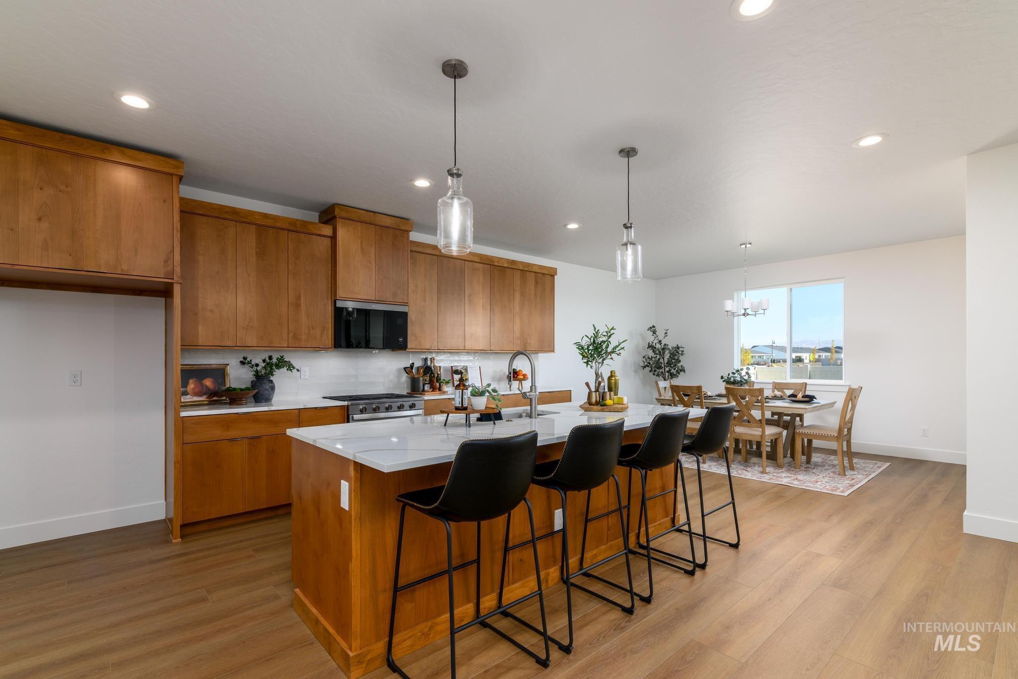 Kitchen featuring brown cabinetry, a breakfast bar area, decorative light fixtures, light stone countertops, and recessed lighting