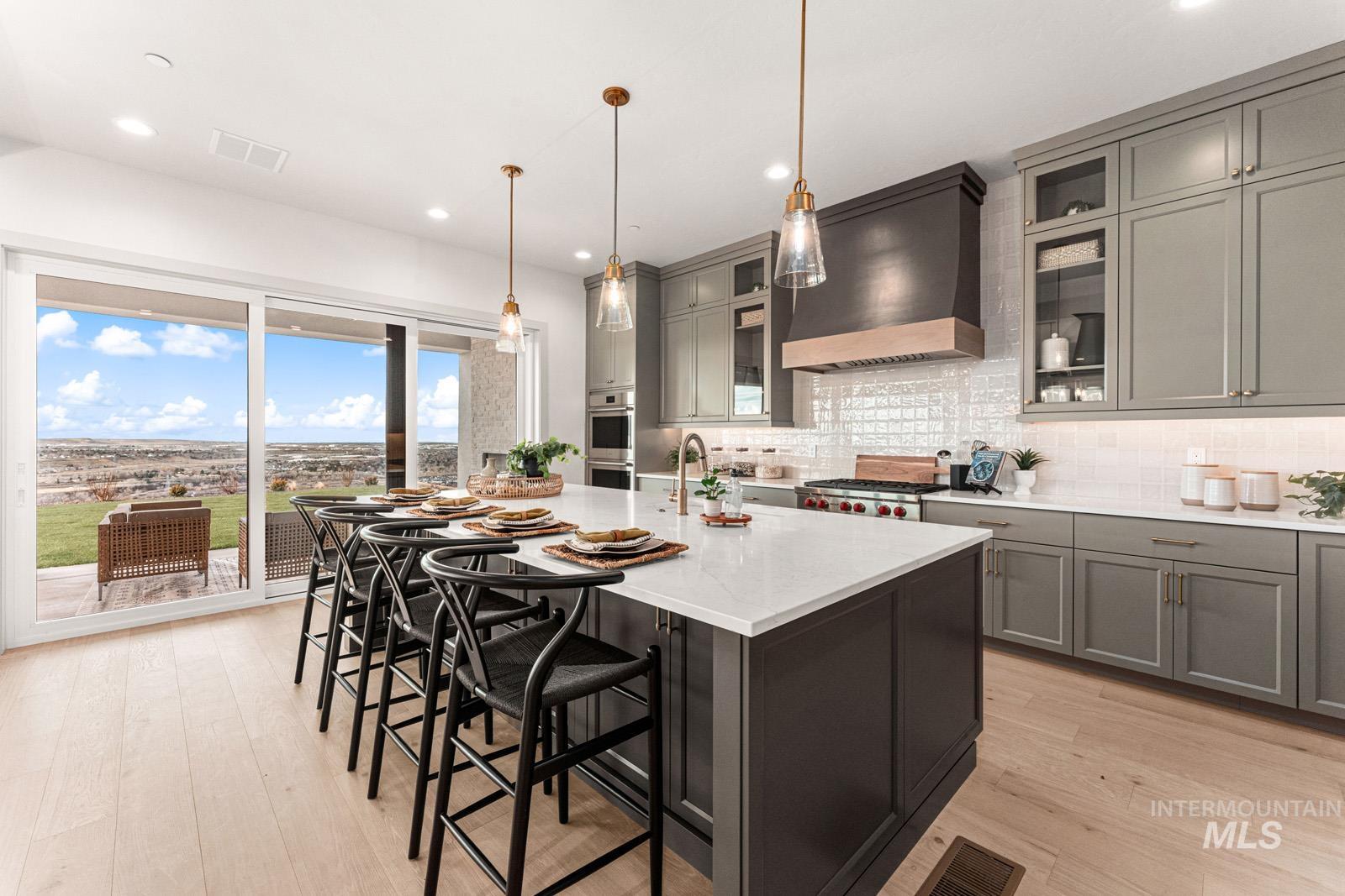 Kitchen featuring gray cabinetry, light wood-style flooring, hanging light fixtures, a kitchen bar, and a center island with sink