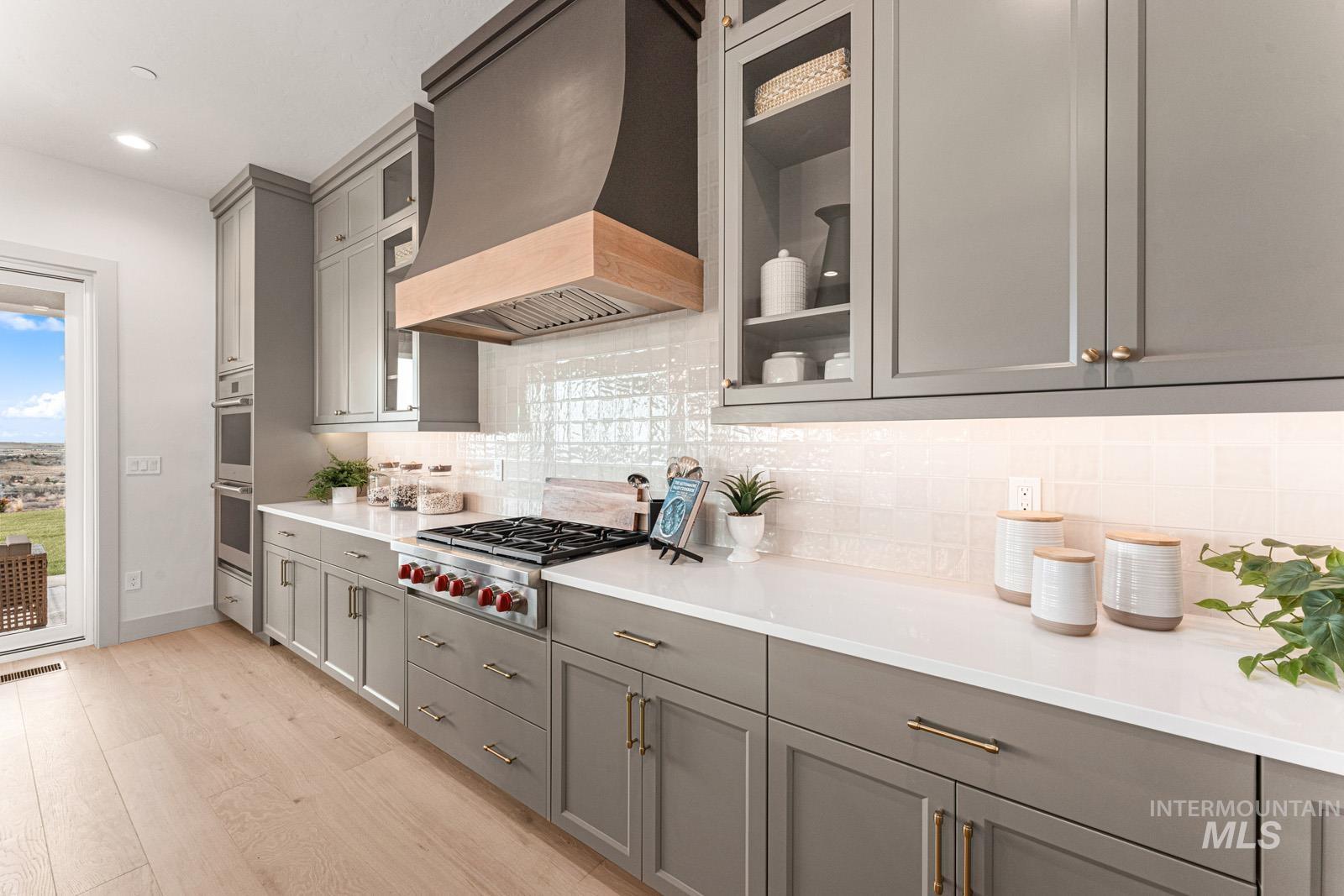 Kitchen with gray cabinetry, light wood-style floors, stainless steel appliances, glass fronted cabinets, and recessed lighting