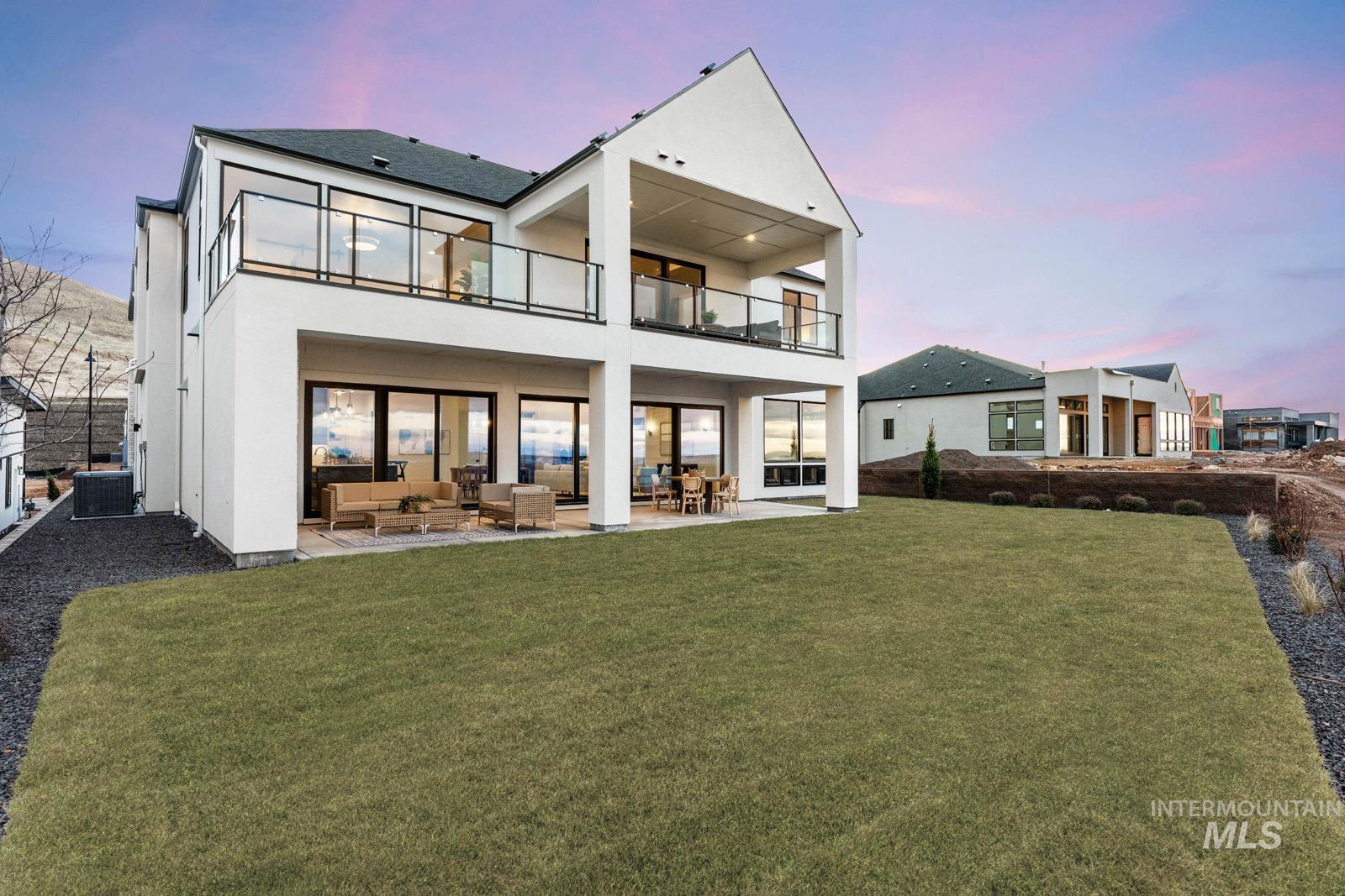 Back of house at dusk featuring a patio area, a lawn, a balcony, outdoor seating, and stucco siding