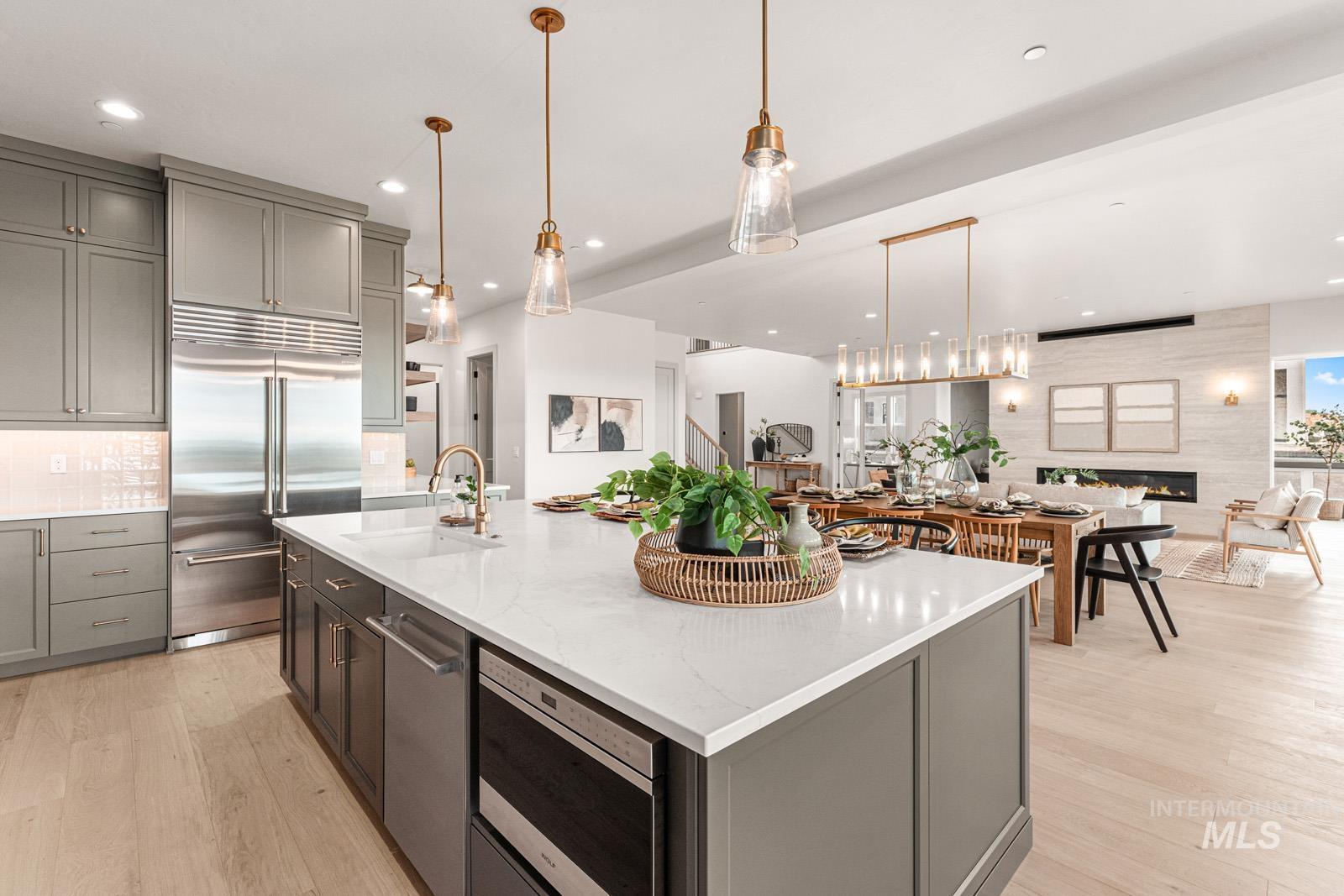 Kitchen featuring pendant lighting, built in appliances, light stone counters, gray cabinetry, and light wood-style floors