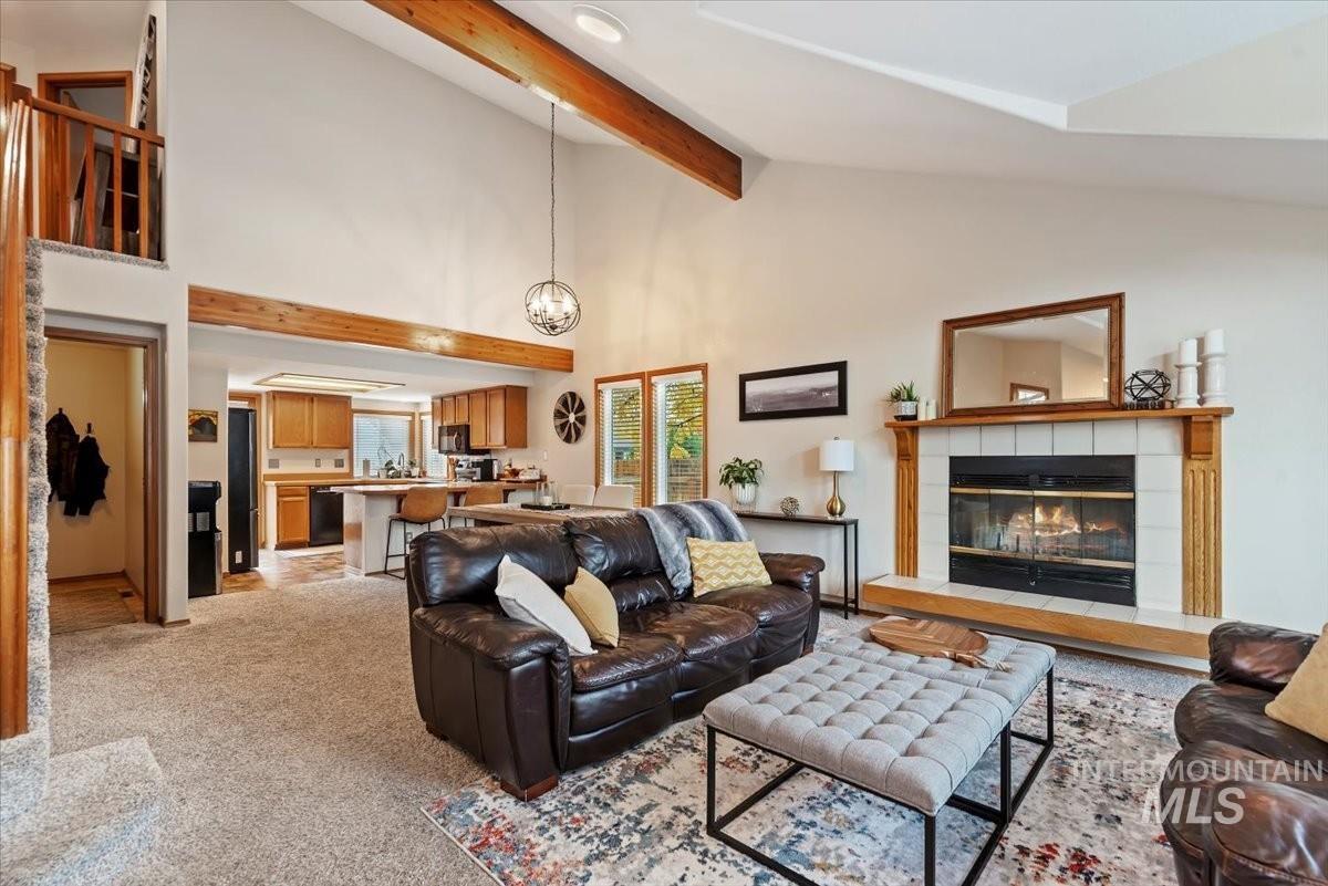Living room with high vaulted ceiling, beam ceiling, light colored carpet, a fireplace, and a chandelier