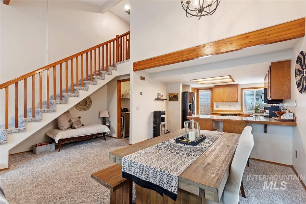 Dining area featuring beam ceiling, light carpet, a high ceiling, and stairs