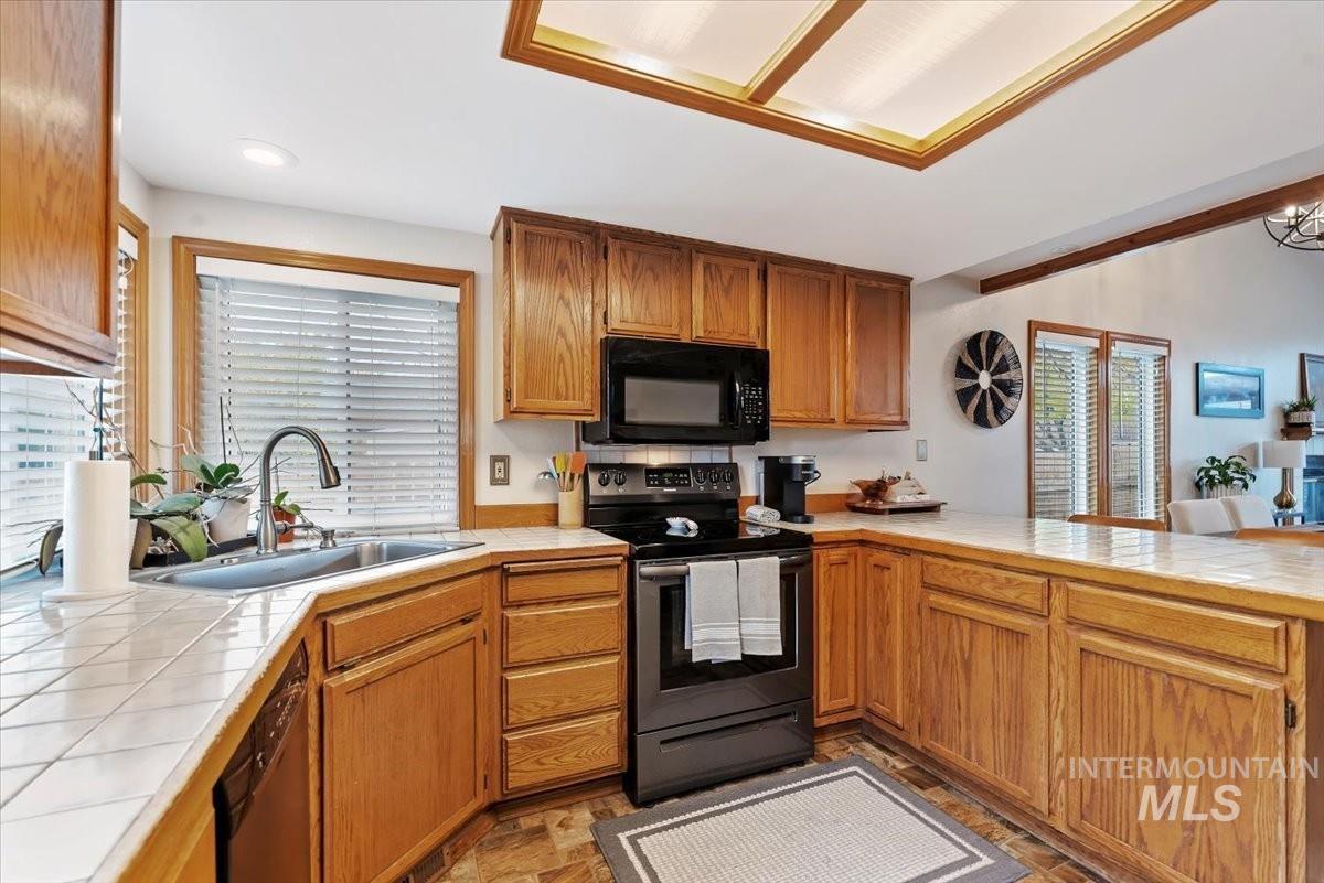 Kitchen featuring tile countertops, black appliances, brown cabinets, stone finish floors, and a peninsula