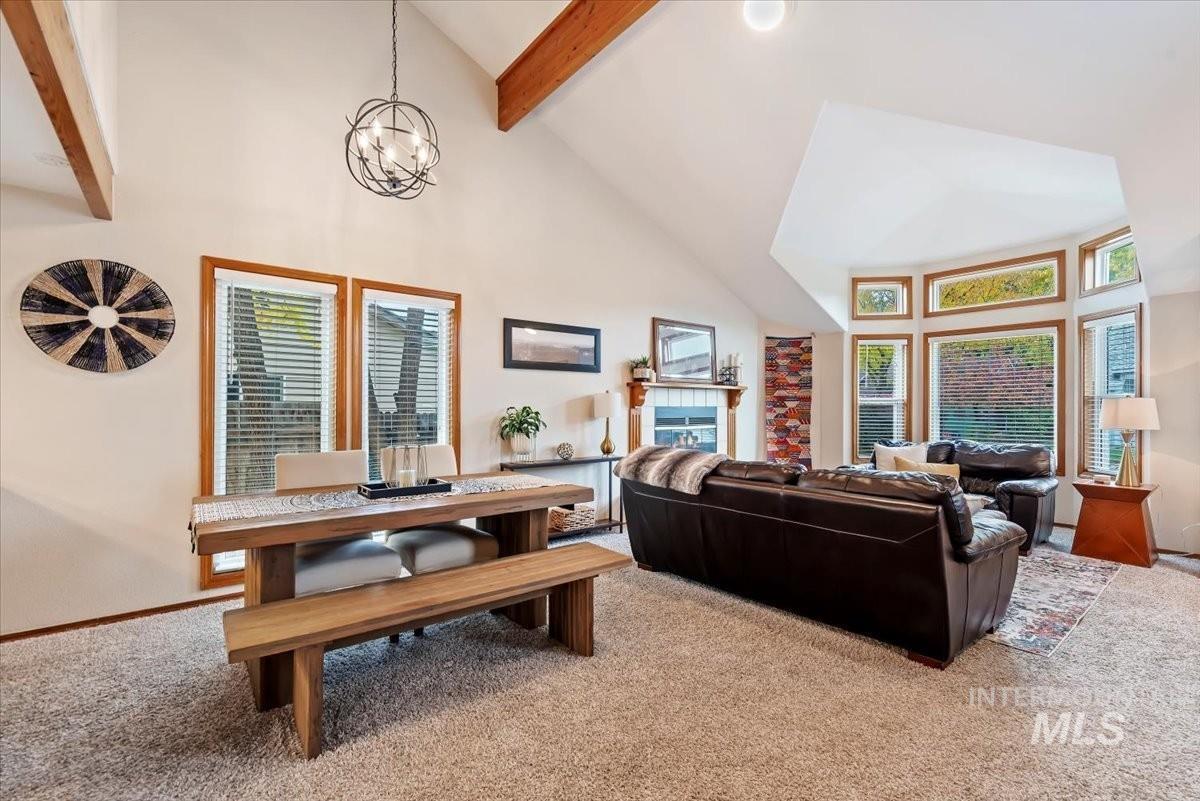 Living room with carpet, high vaulted ceiling, beamed ceiling, a chandelier, and a tiled fireplace