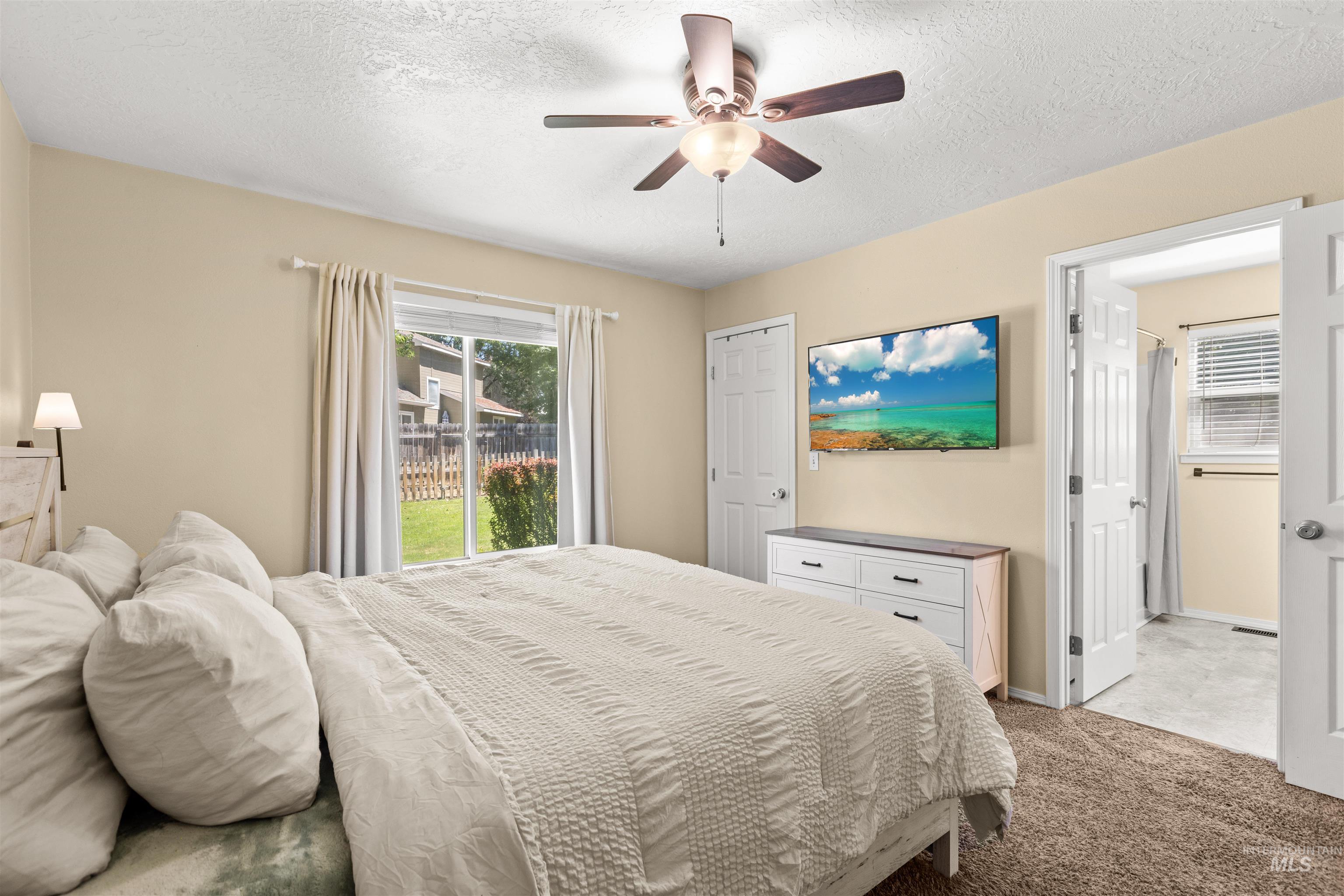 Carpeted bedroom featuring a ceiling fan, a window with exterior views, and an open doorway to a bathroom