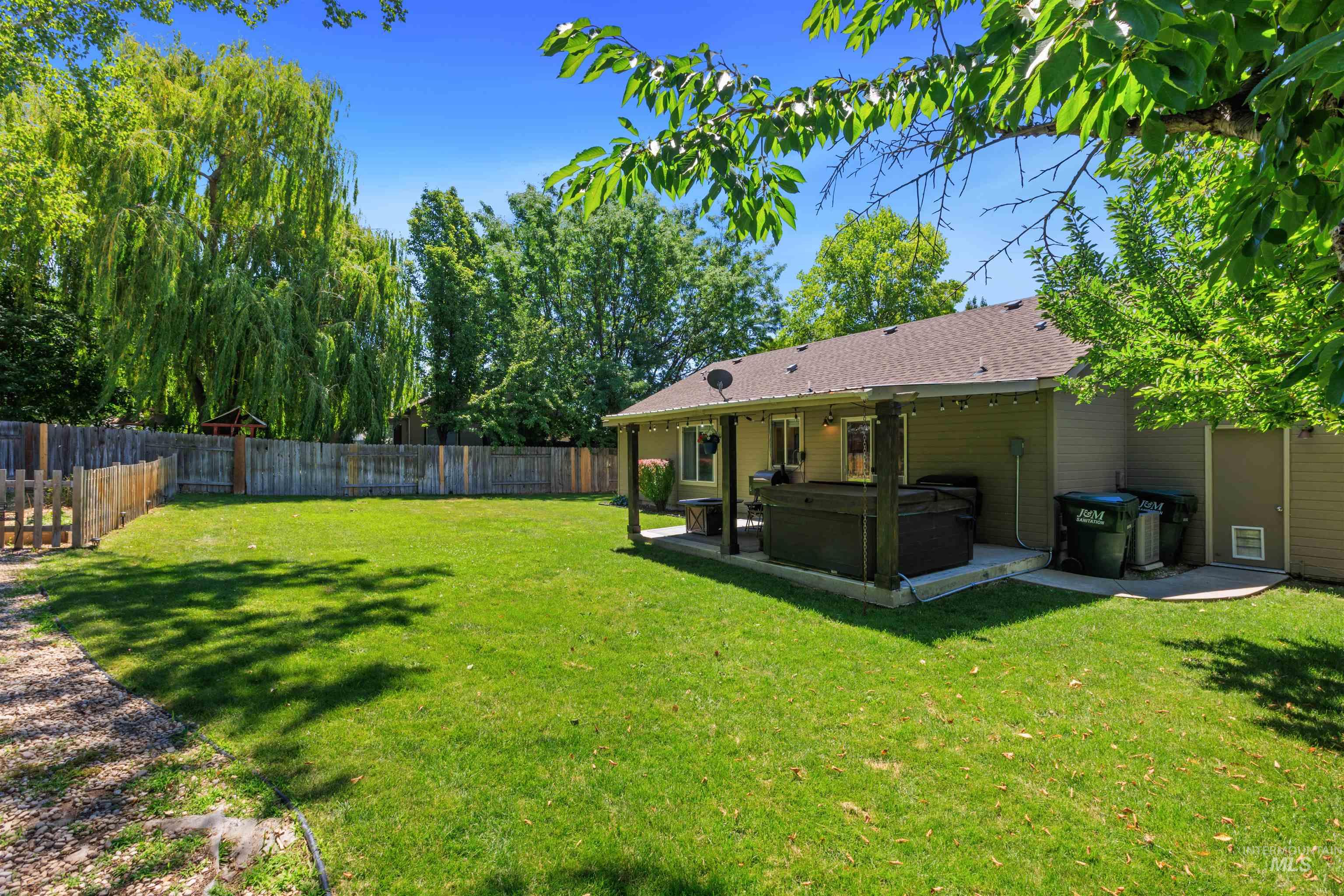 Expansive backyard featuring a manicured lawn, a full wooden privacy fence, and mature trees