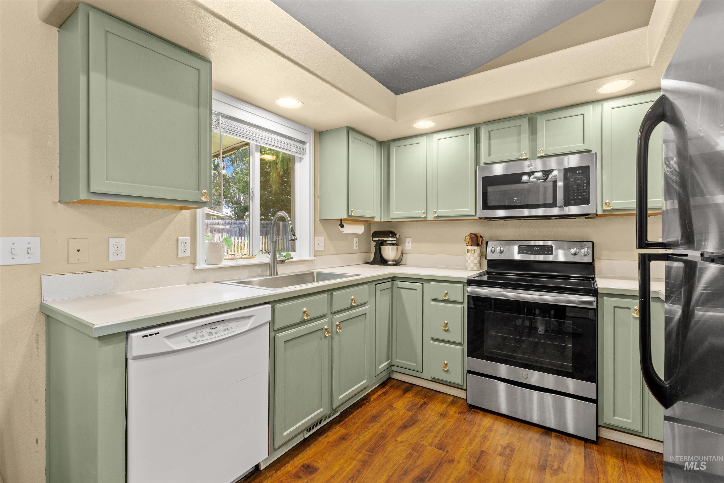 Kitchen featuring sage green cabinetry, light-toned countertops, stainless steel appliances, wood-finish flooring, and recessed lighting