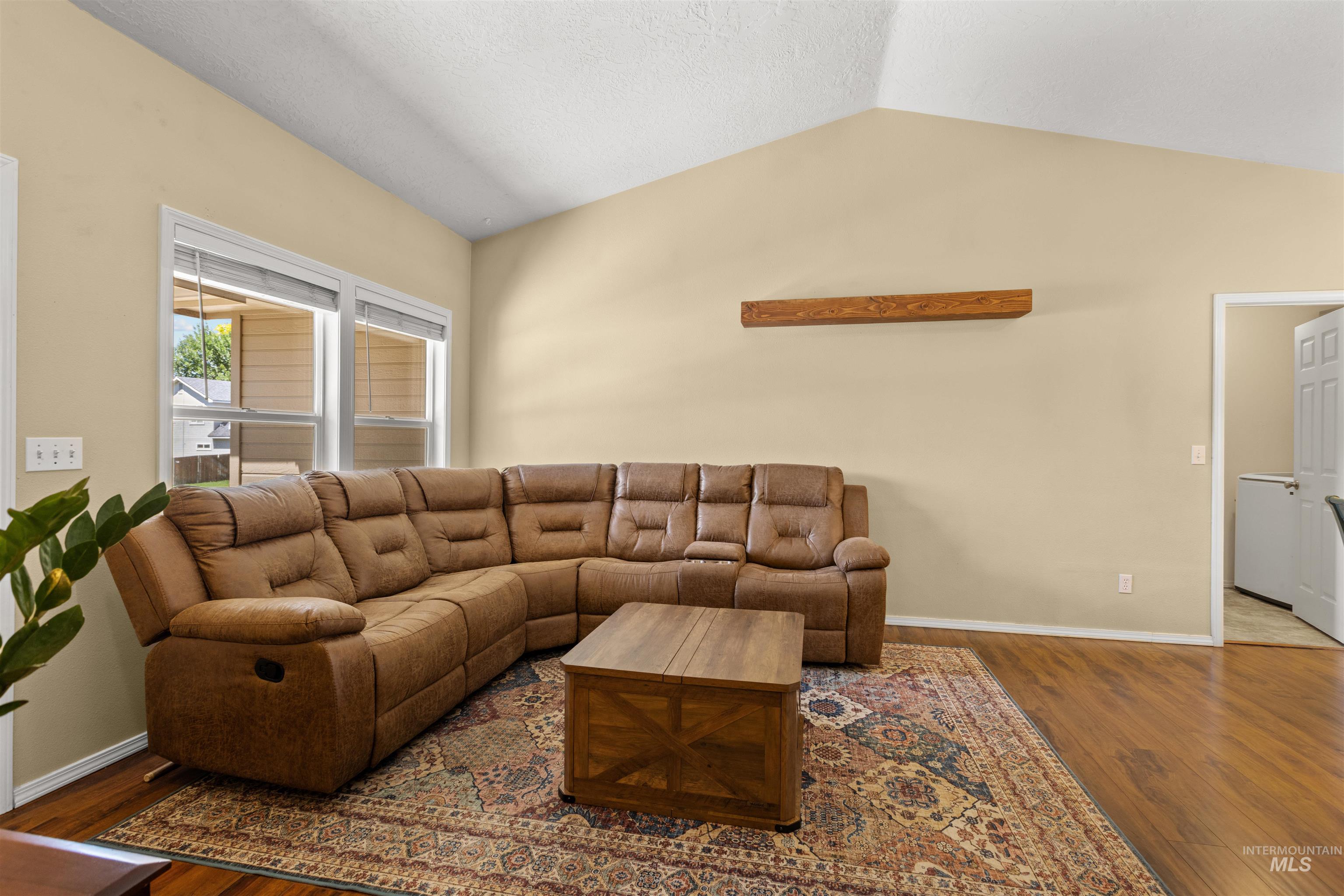 Living area featuring vaulted ceilings, wood-finish flooring, and a decorative floating shelf