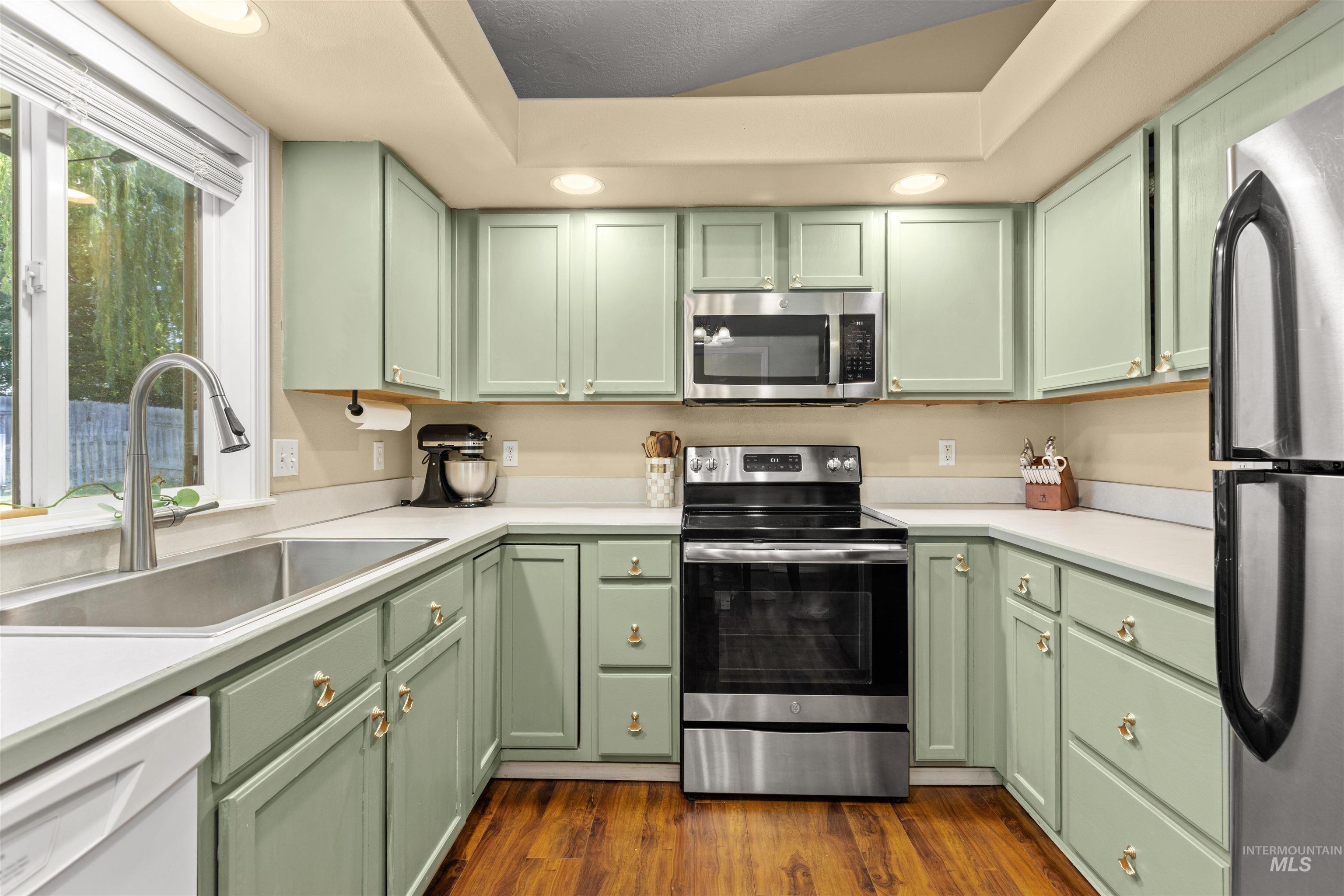 Kitchen featuring light green cabinetry, stainless steel appliances, wood-finish flooring, recessed lighting, and a window over the sink