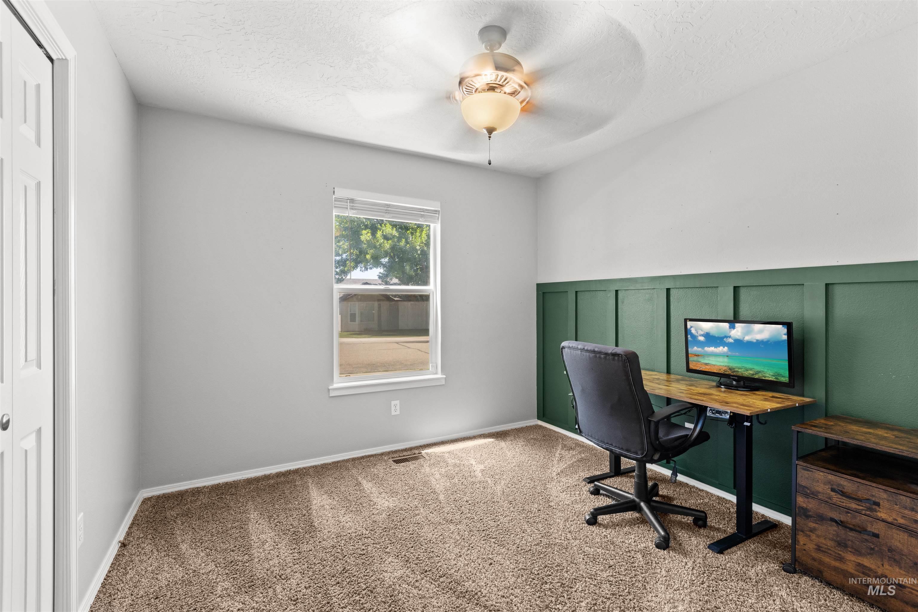 Bedroom featuring a green board and batten accent wall, neutral carpeting, a single window with blinds, a ceiling fan, and bi-fold closet doors
