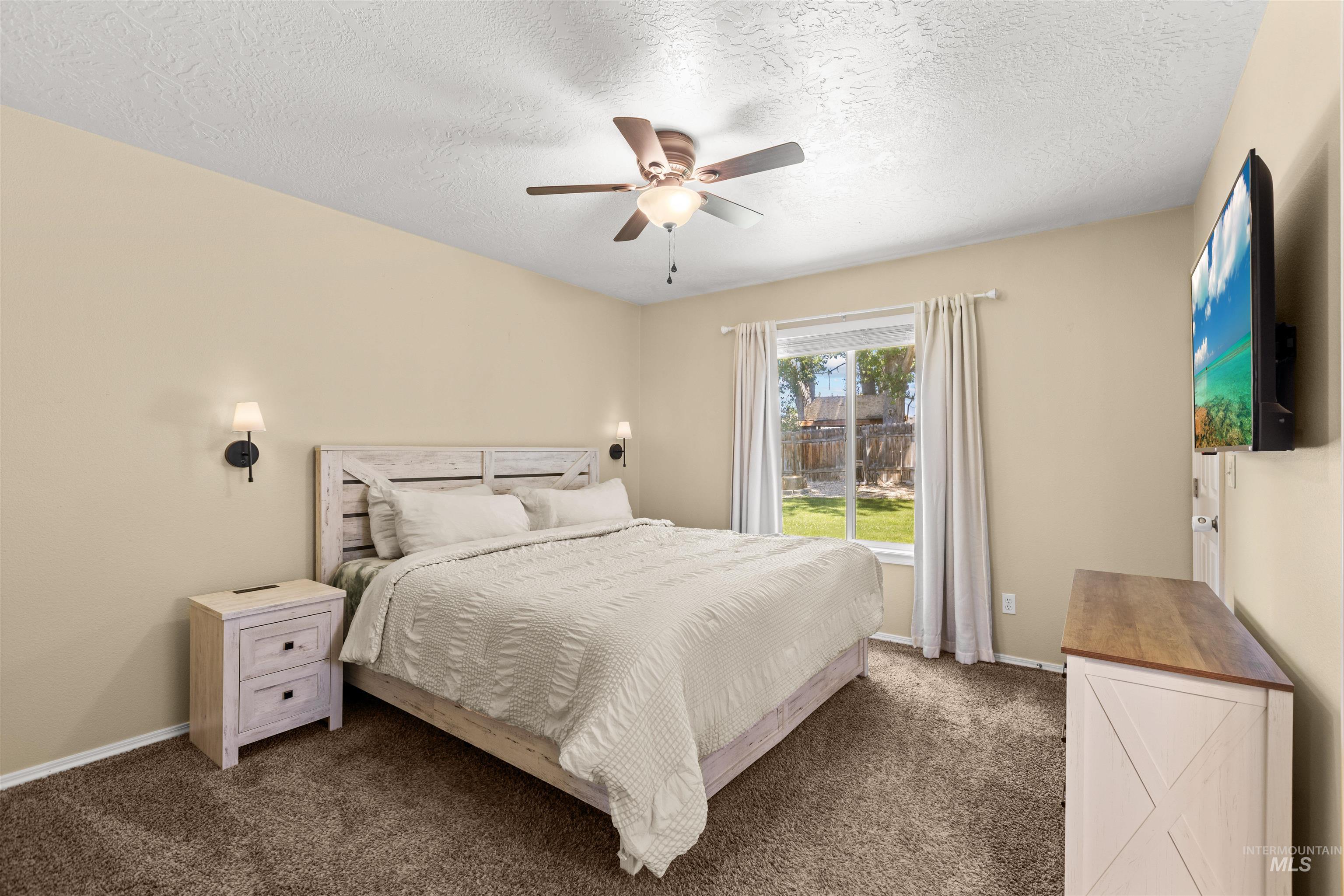 Carpeted room with a ceiling fan, sconce lighting, and a window providing natural illumination and outdoor views