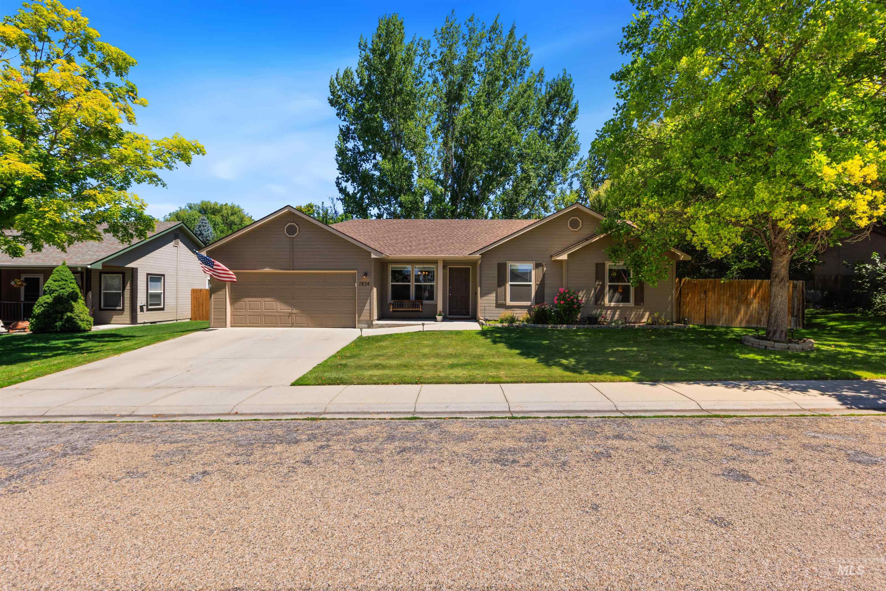 Single-story residence featuring a two-car garage, concrete driveway, and a front yard with mature trees