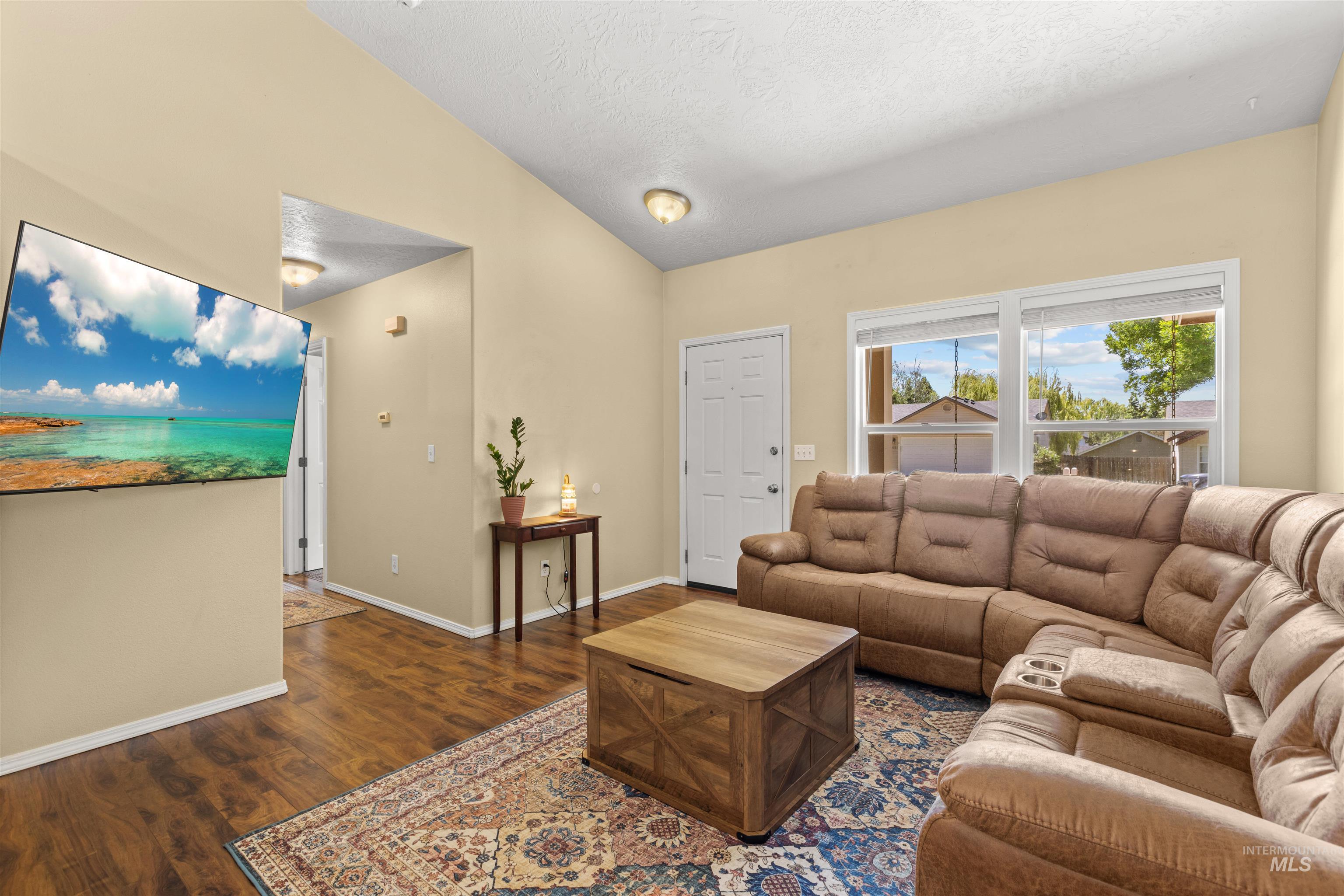 Living area featuring wood-finish flooring, vaulted ceiling, and ample natural light through a double window