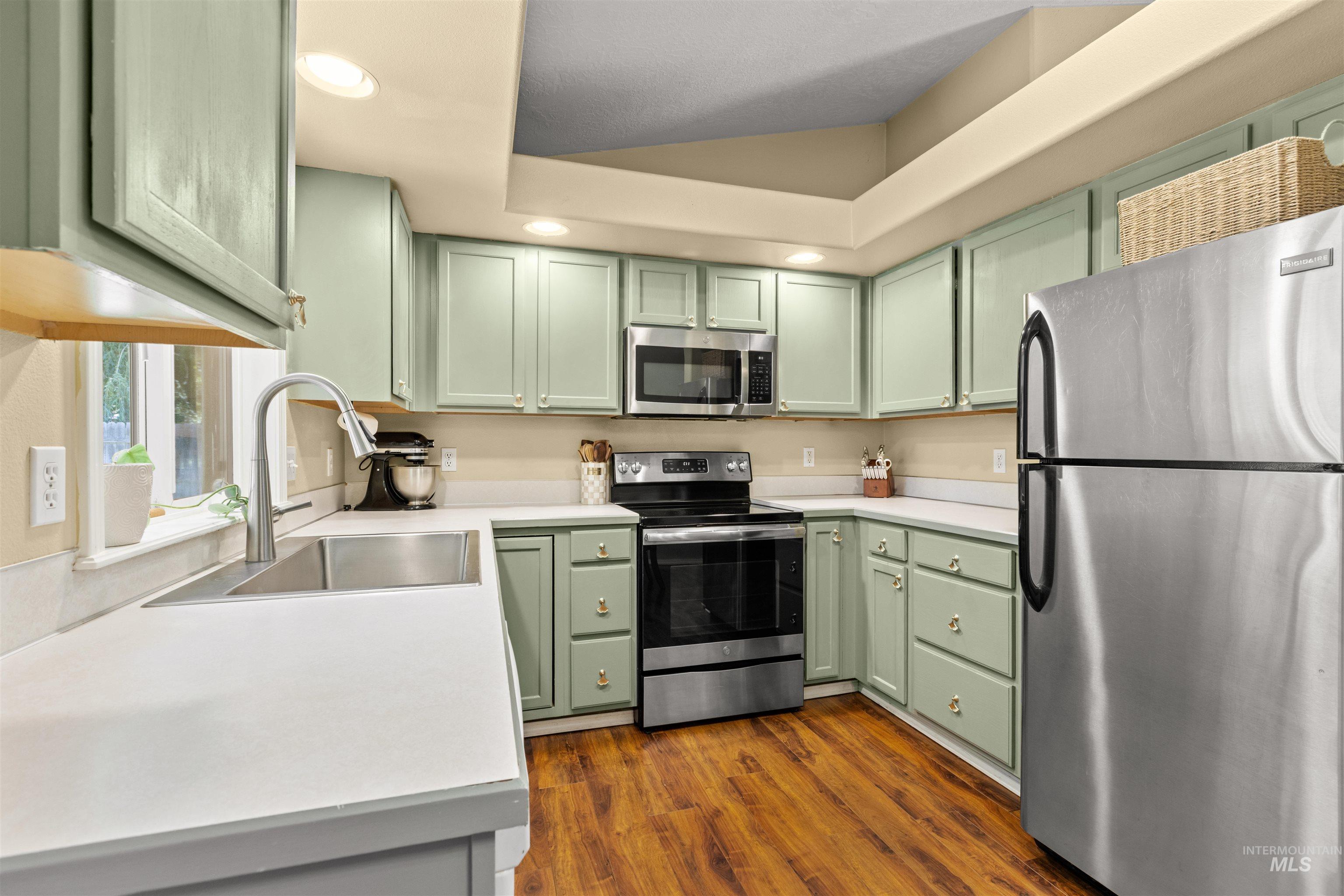 Kitchen featuring light green cabinetry, white countertops, stainless steel appliances, and wood-finish flooring