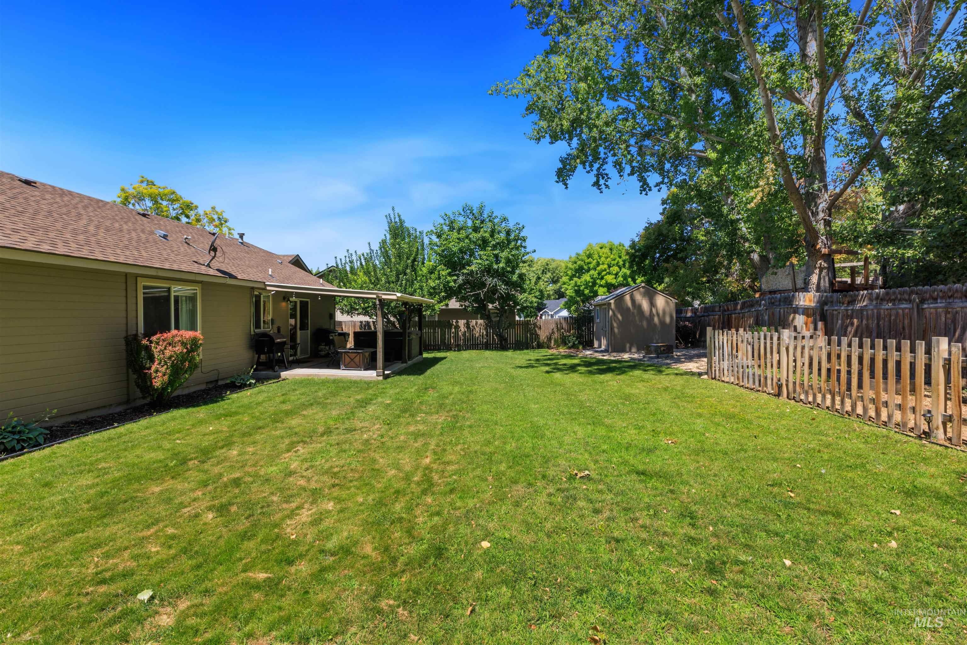 Expansive backyard featuring a large green lawn, covered patio, and a separate storage shed