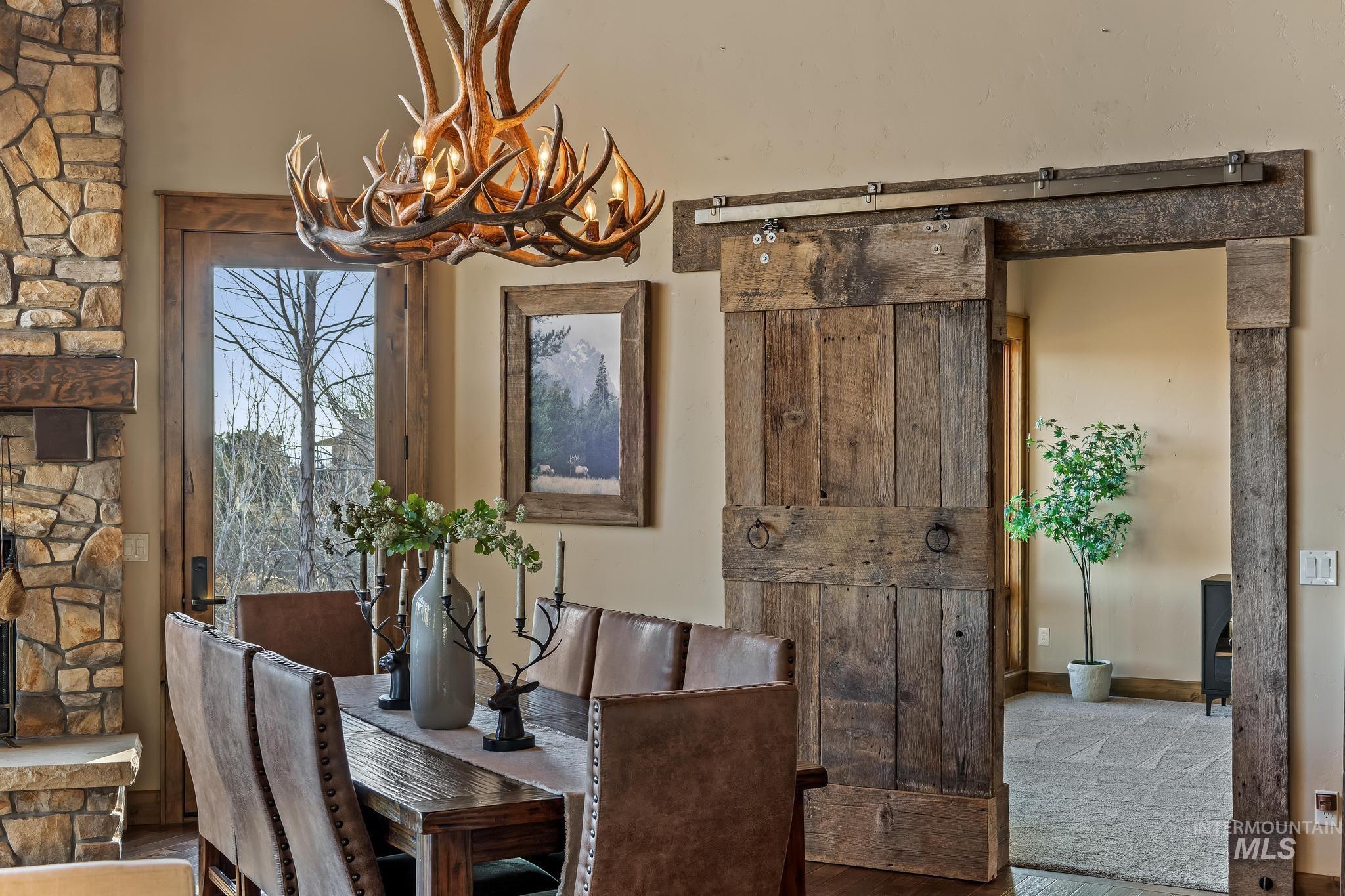 Dining area with custom lighting, front patio access, hickory wood floors, stone fireplace, and reclaimed wood barn door