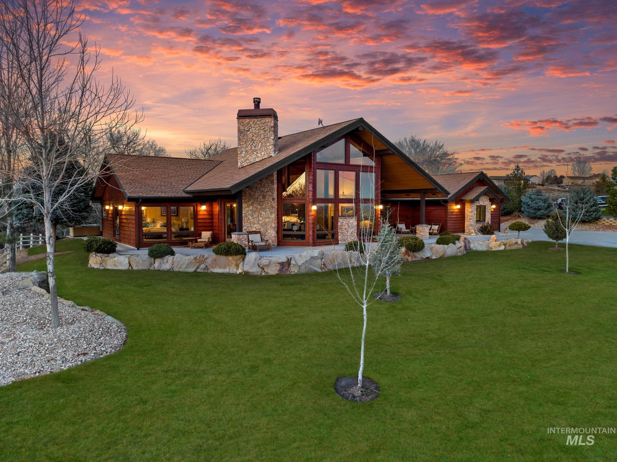 Front of property at dusk with a lawn, a patio, stone siding, and a chimney