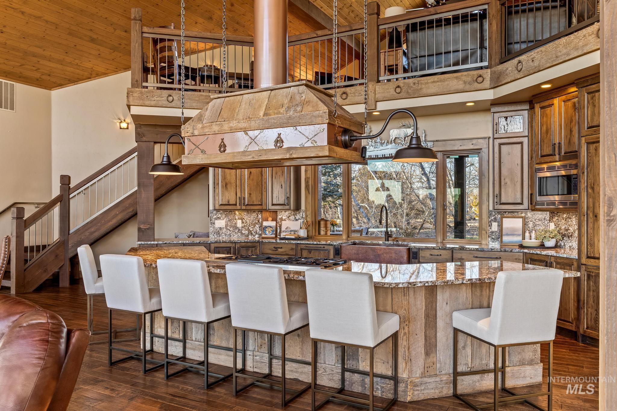 Kitchen with large entertaining island wrapped with antique reclaimed barnwood, custom wood cabinetry, granite counter and backsplash, Custom range hood, peaked ceiling
