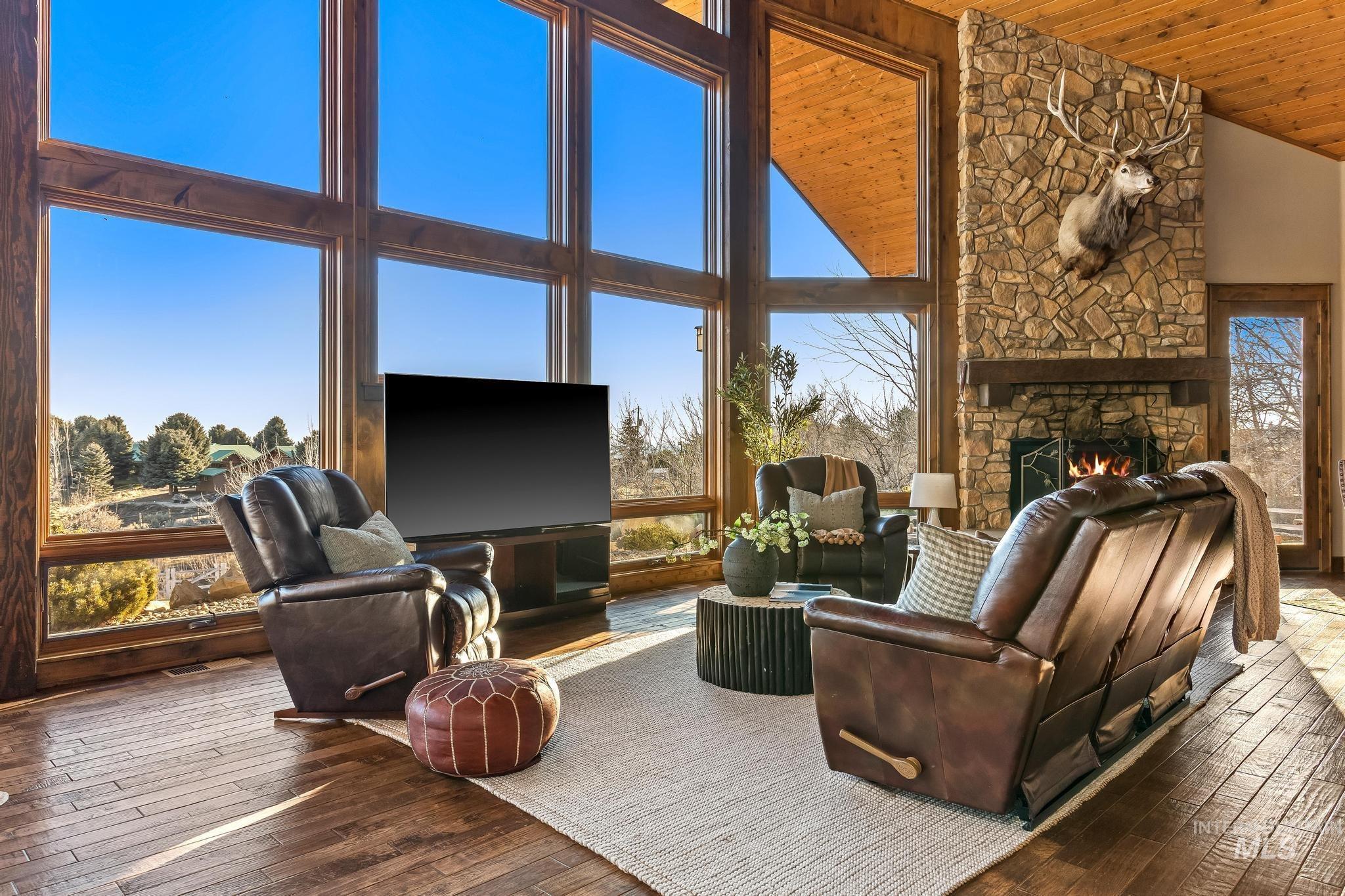 Great Room with a vaulted wood beamed ceiling, floor-to-ceiling stone fireplace, wall of wood cased windows