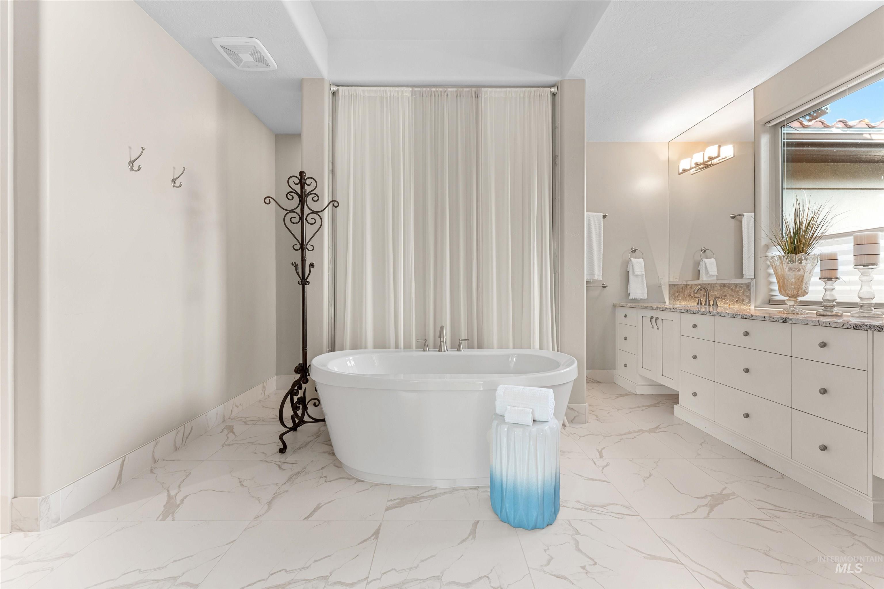 Full bath featuring vanity, a freestanding tub, and light marble finish flooring