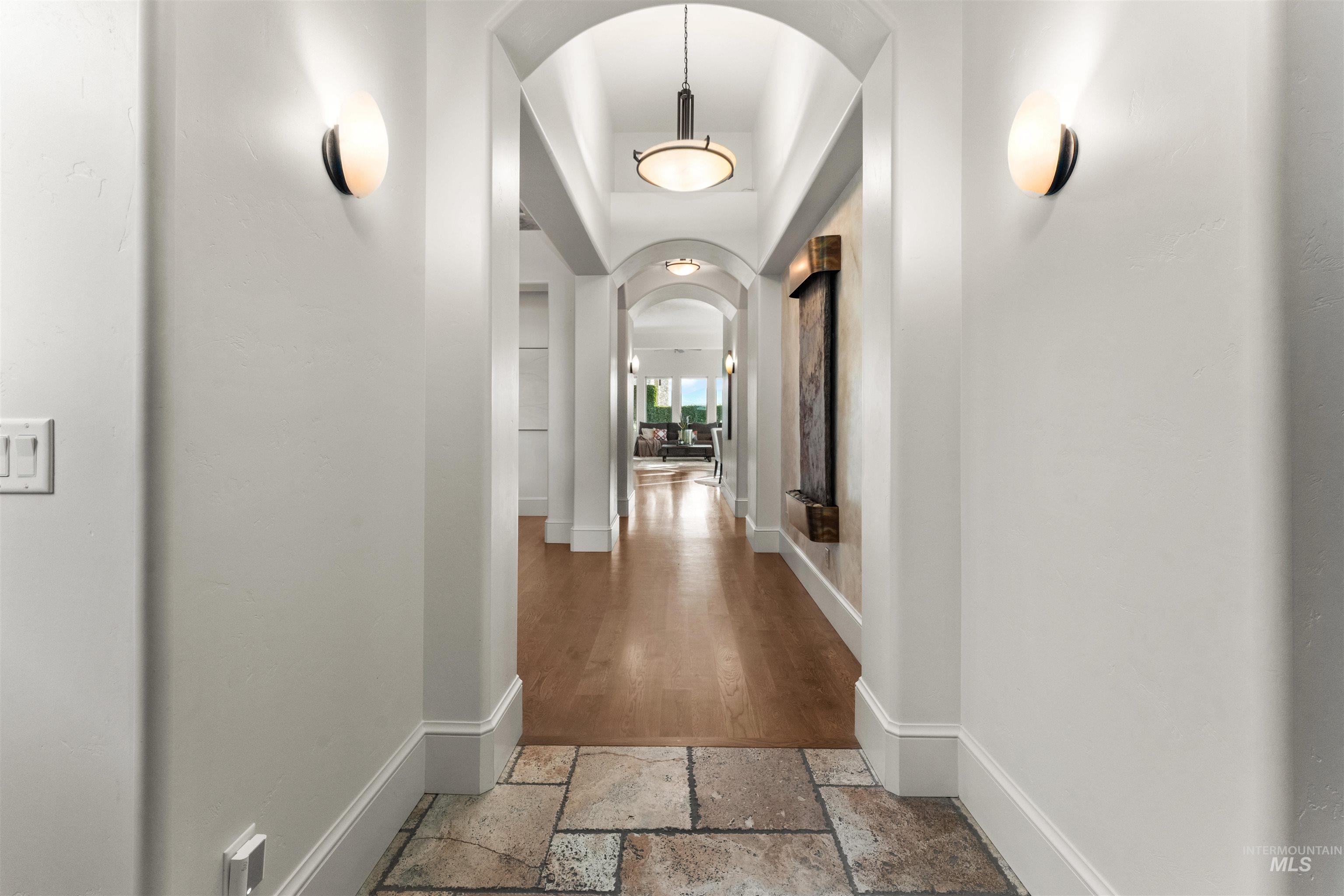 Corridor with arched walkways, stone tile floors, and a tray ceiling