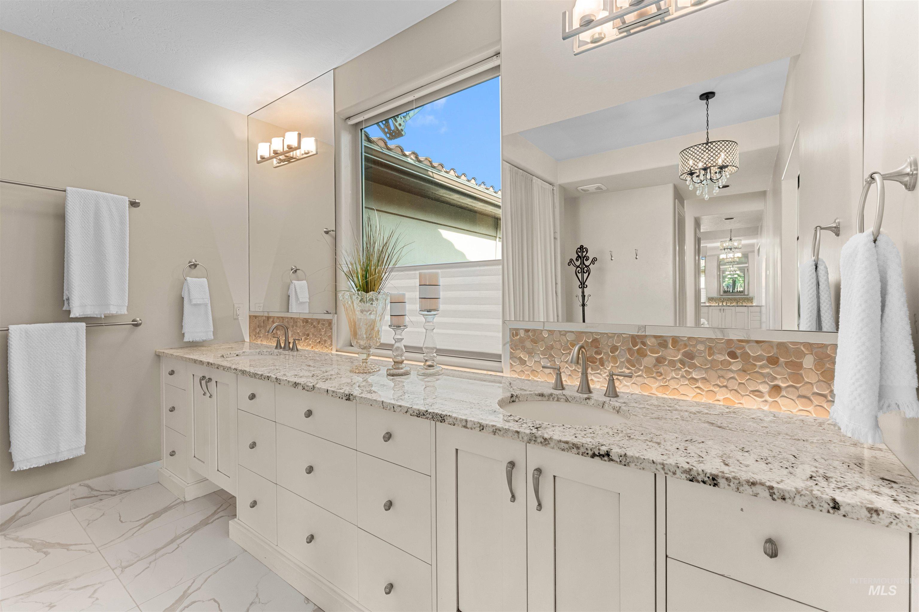 Full bathroom with a chandelier, double vanity, plenty of natural light, and decorative backsplash