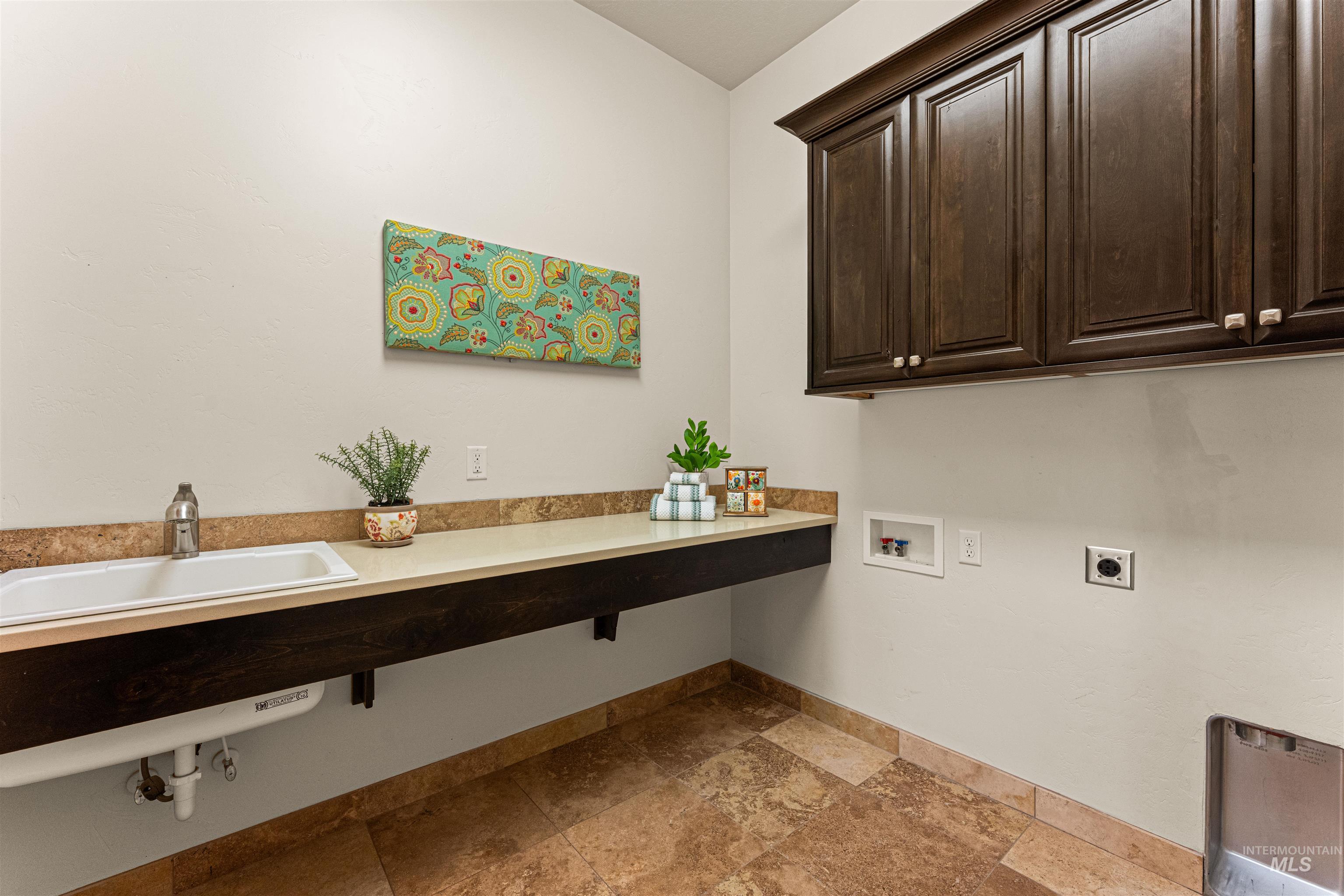 Laundry area with hookup for an electric dryer, hookup for a washing machine, cabinet space, and stone tile floors