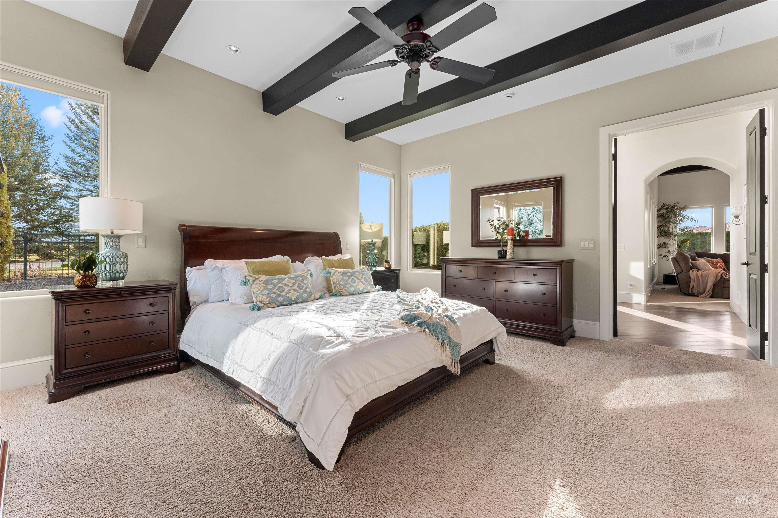 Bedroom with carpet, beamed ceiling, arched walkways, and ceiling fan
