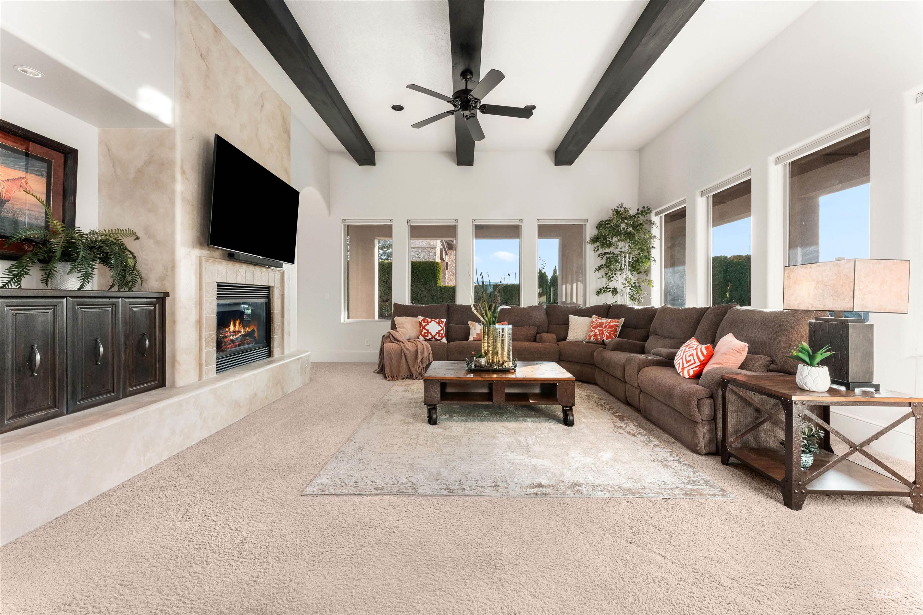 Living room featuring beam ceiling, carpet, a high end fireplace, and ceiling fan
