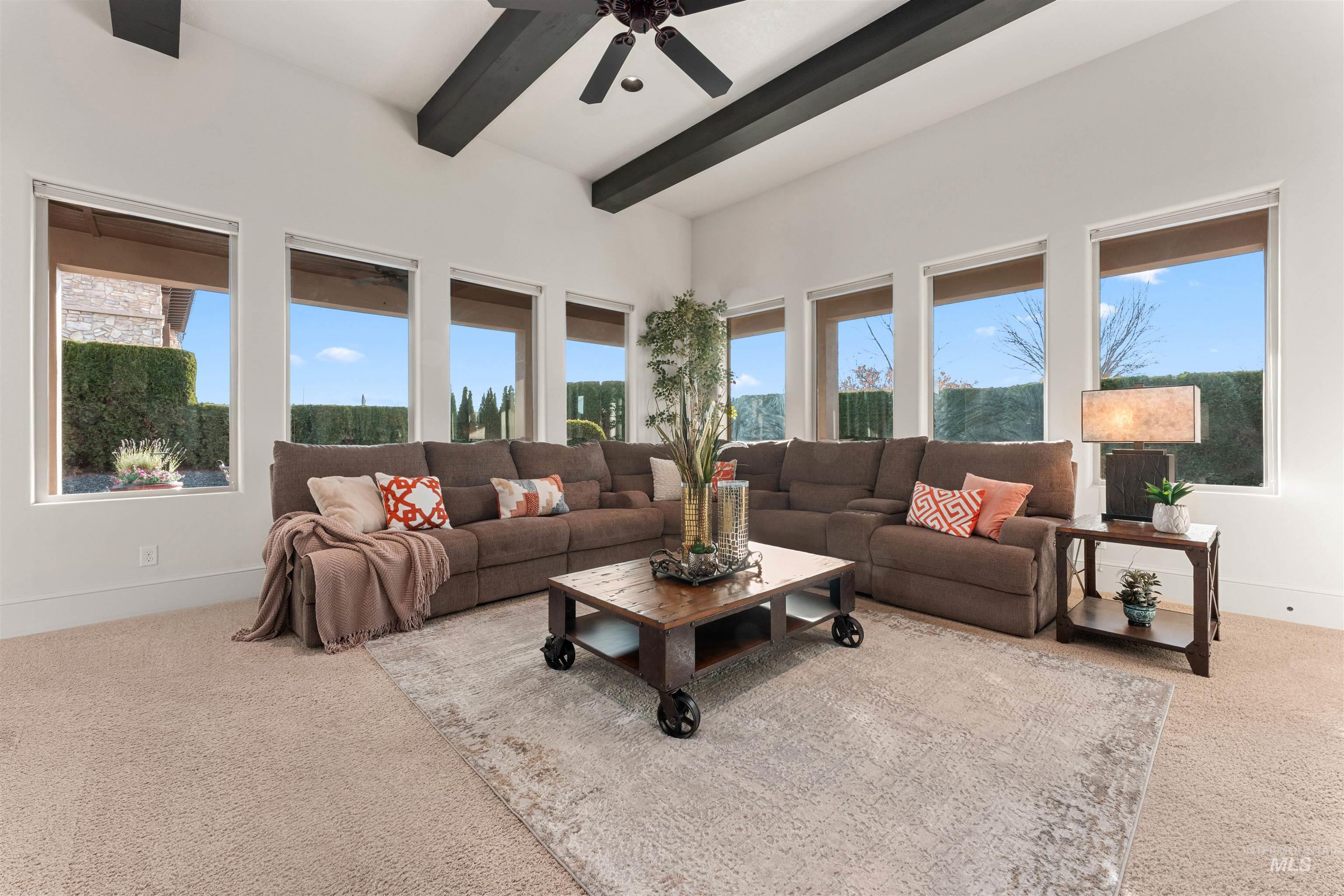 Living room featuring beamed ceiling, light carpet, plenty of natural light, and ceiling fan
