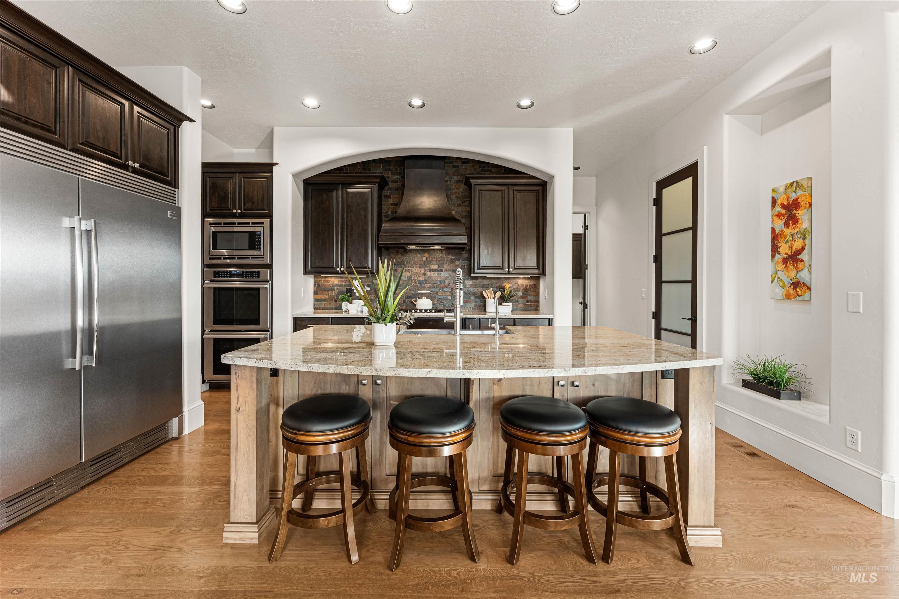Kitchen featuring dark brown cabinetry, built in appliances, light stone counters, recessed lighting, and backsplash