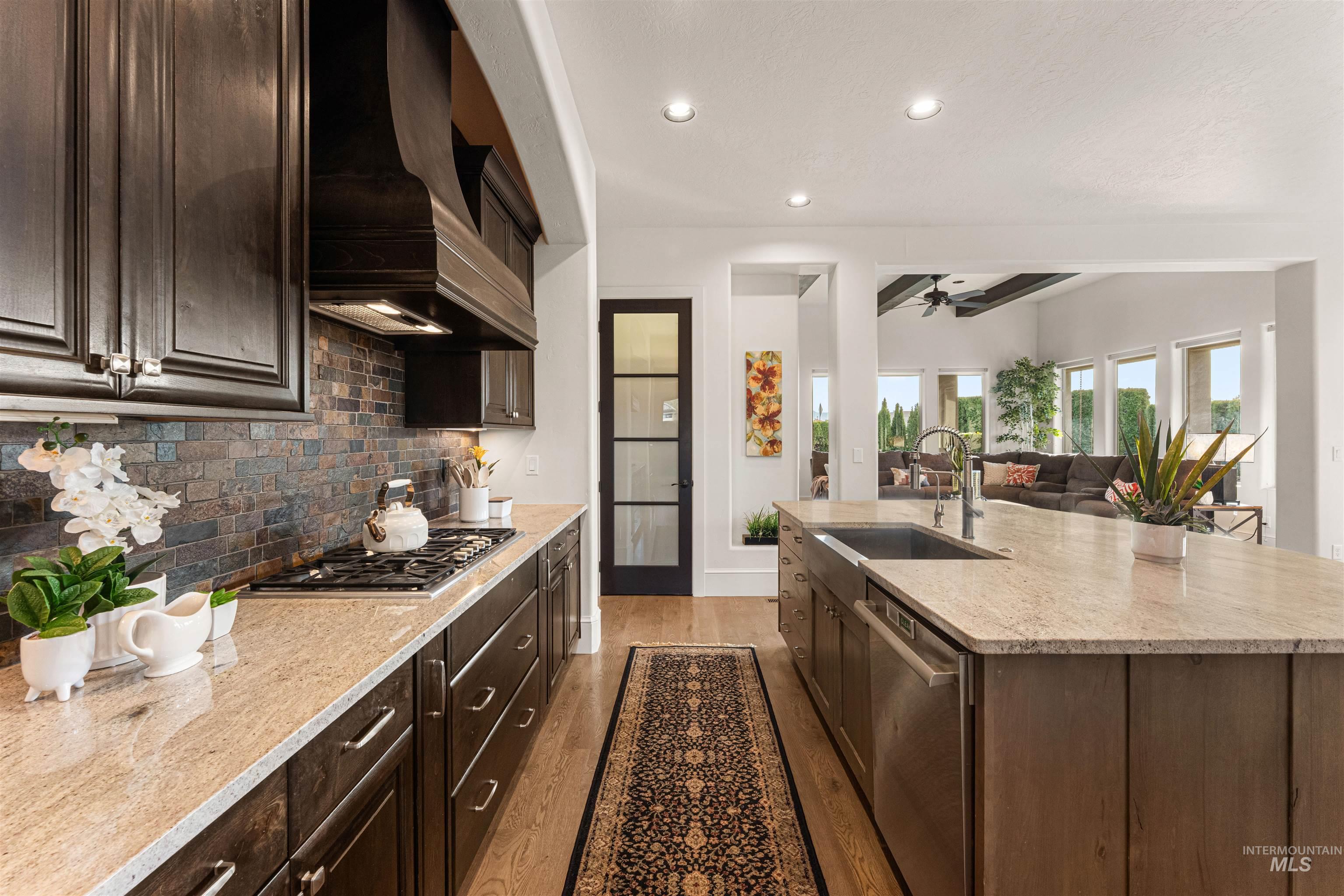 Kitchen featuring dark brown cabinetry, light wood-style flooring, light stone countertops, backsplash, and premium range hood