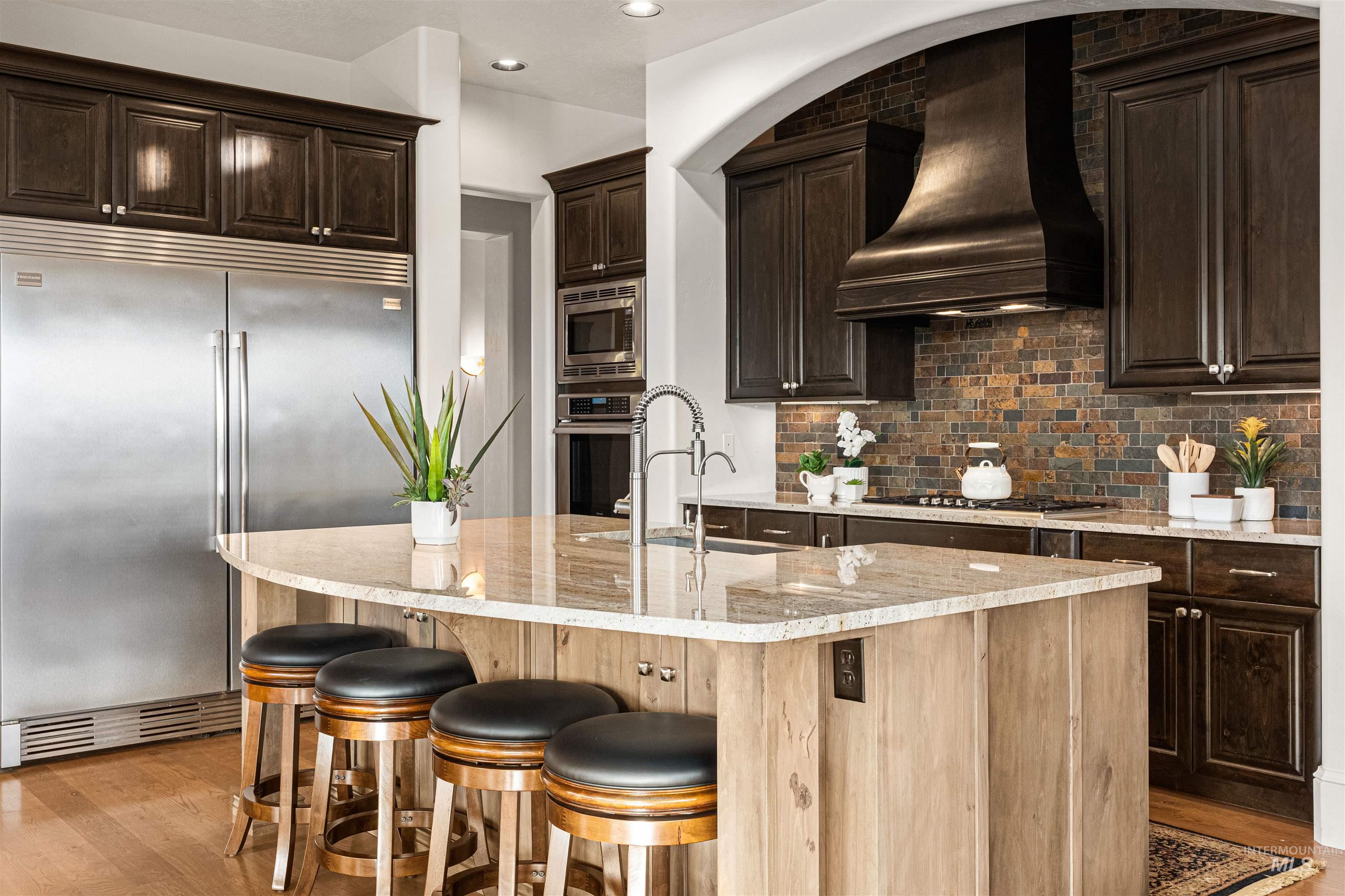 Kitchen with dark brown cabinetry, built in appliances, tasteful backsplash, custom range hood, and light wood finished floors