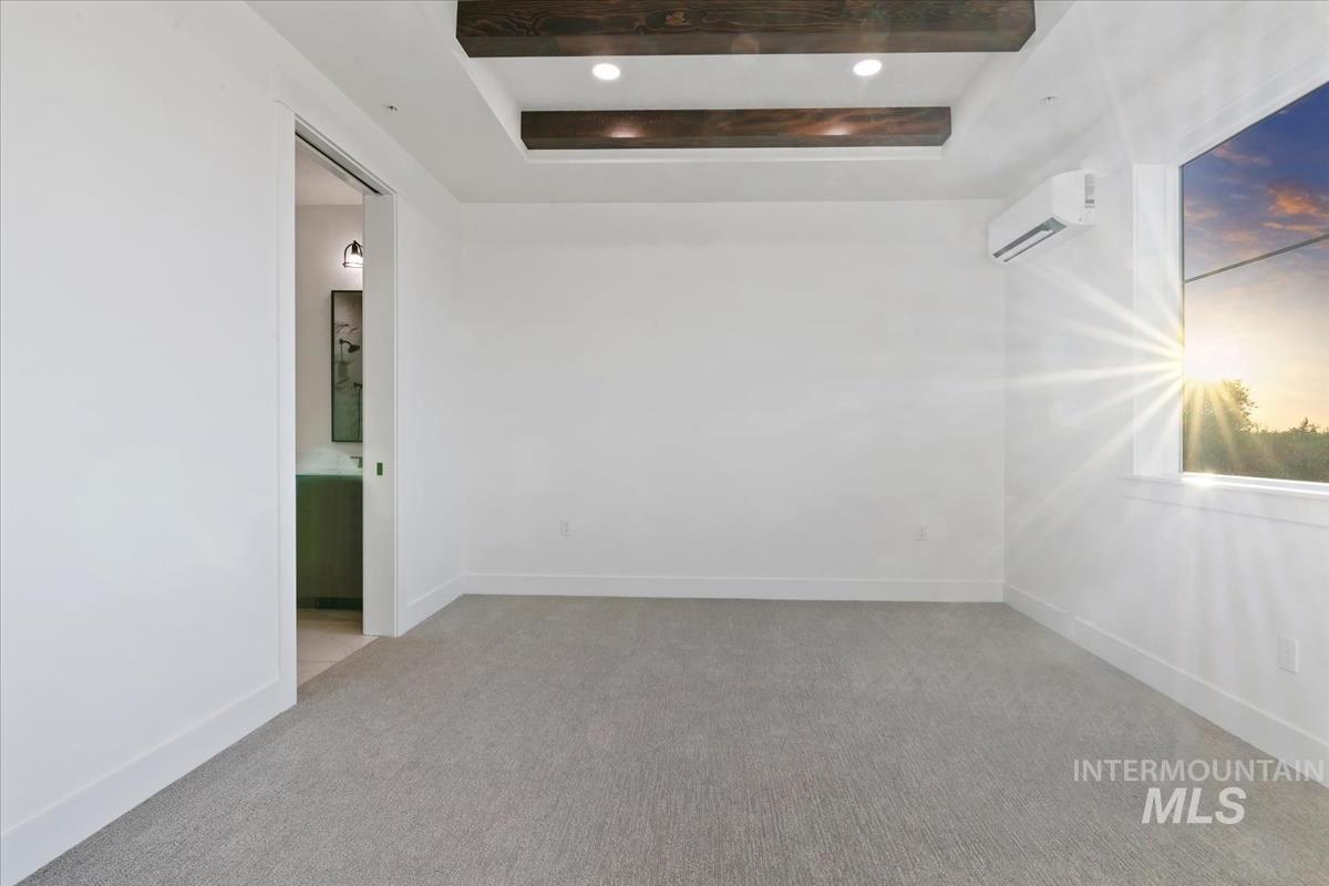 Spare room with a raised ceiling, a wall unit AC, and light colored carpet