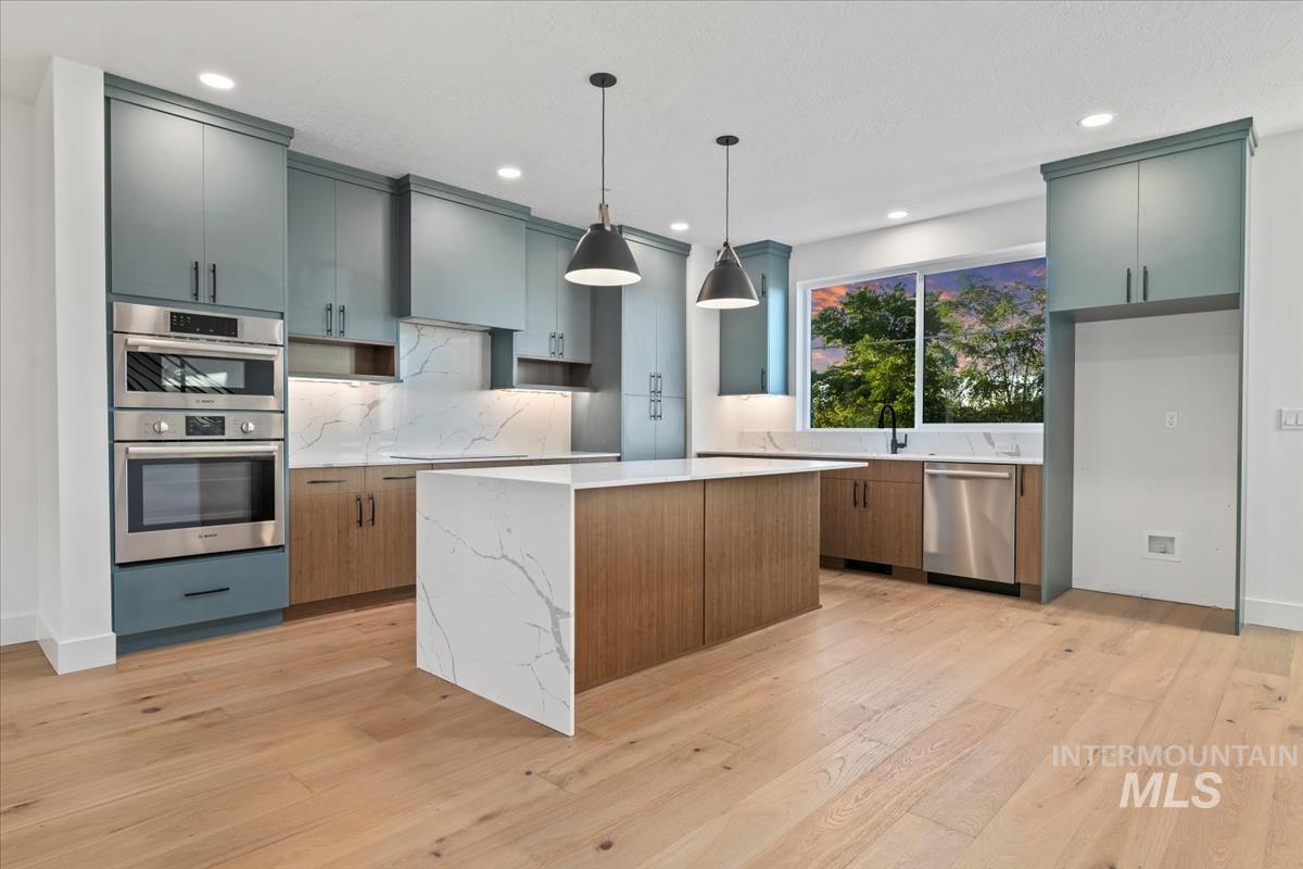 Kitchen with a kitchen island, decorative light fixtures, light wood finished floors, light stone counters, and stainless steel appliances