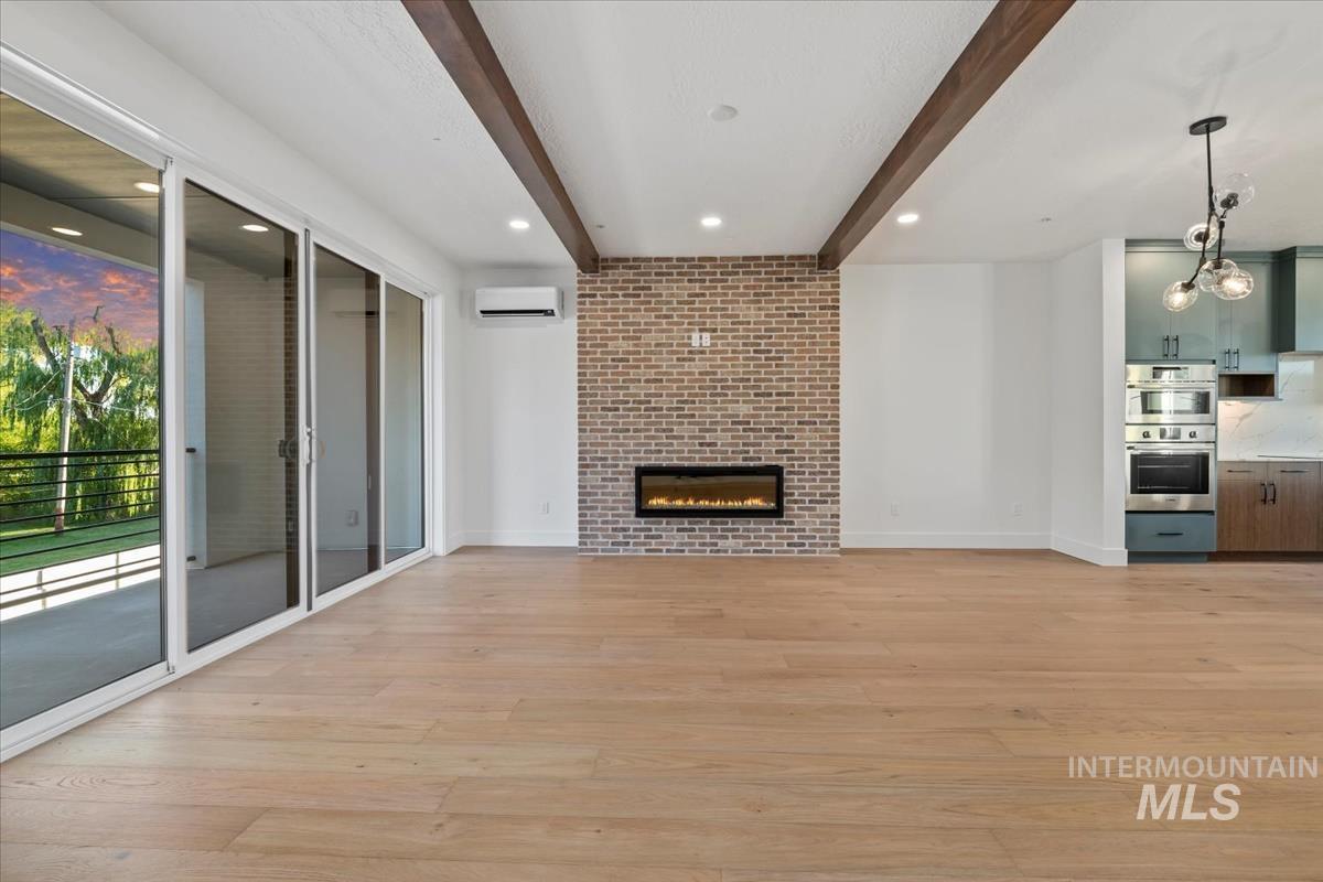 Unfurnished living room with recessed lighting, light wood finished floors, beamed ceiling, a brick fireplace, and a wall unit AC