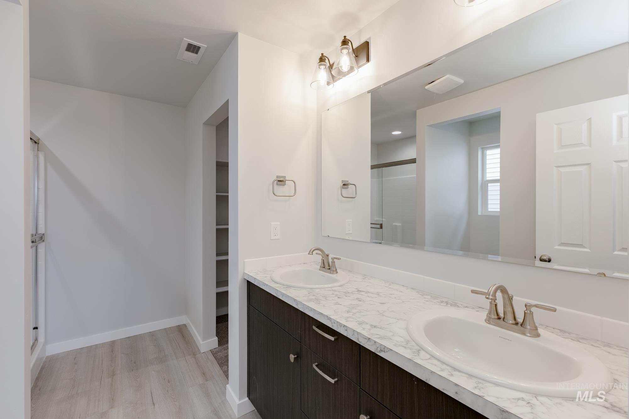 Full bathroom with double vanity, a shower stall, light wood-type flooring, and a walk in closet