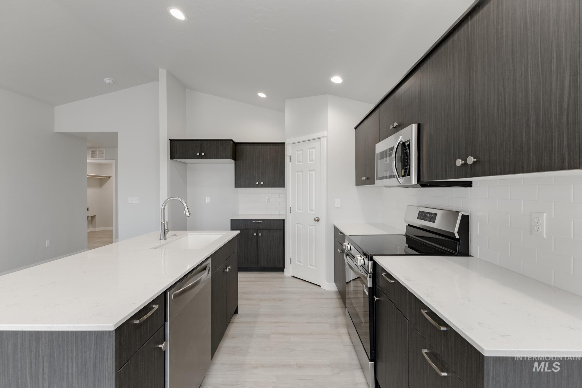 Kitchen featuring appliances with stainless steel finishes, light stone countertops, tasteful backsplash, a kitchen island with sink, and lofted ceiling