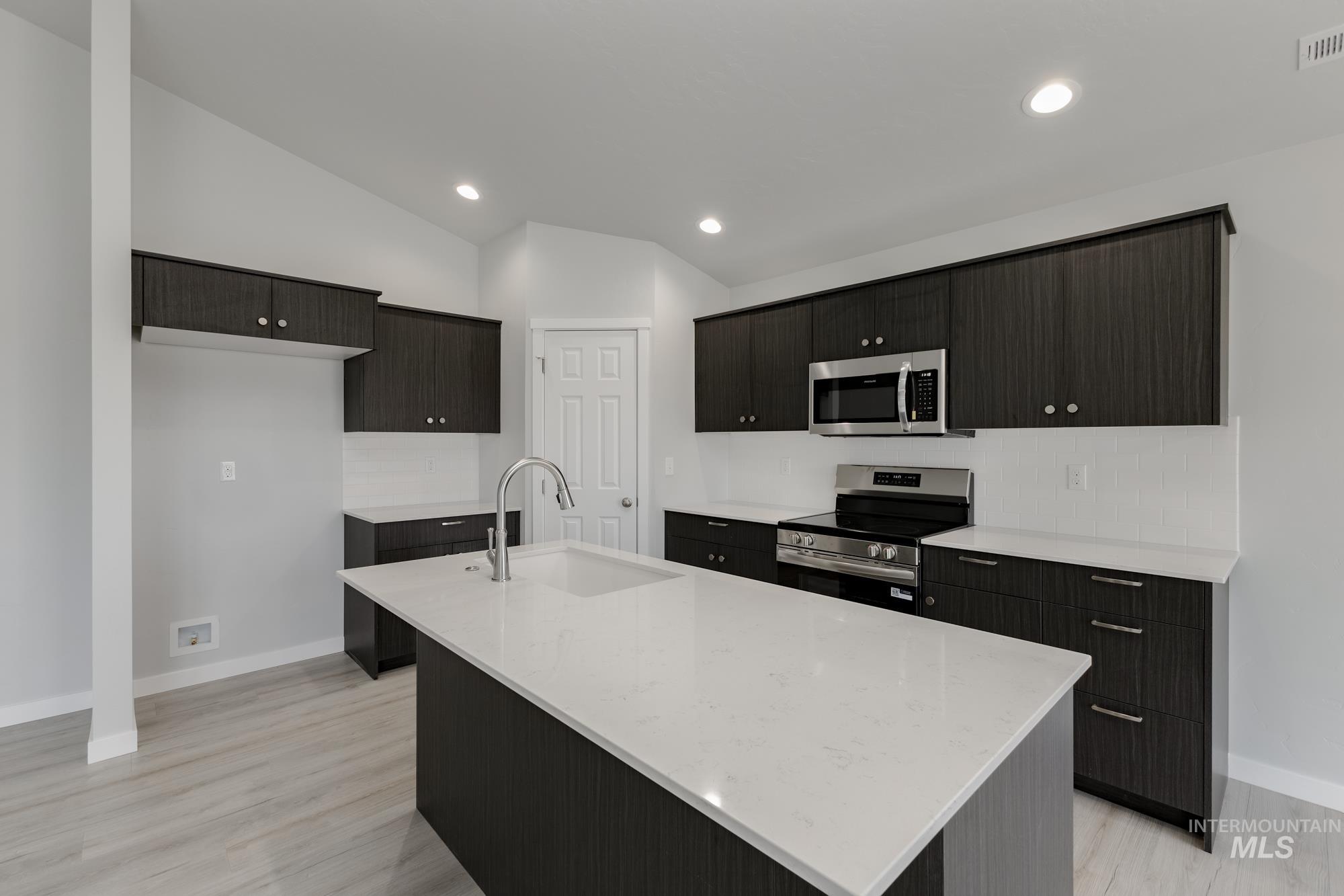 Kitchen with stainless steel appliances, light stone countertops, a kitchen island with sink, recessed lighting, and vaulted ceiling