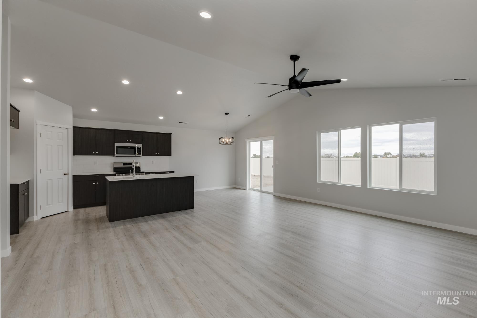 Kitchen with open floor plan, dark cabinets, a kitchen island with sink, lofted ceiling, and light wood-style floors